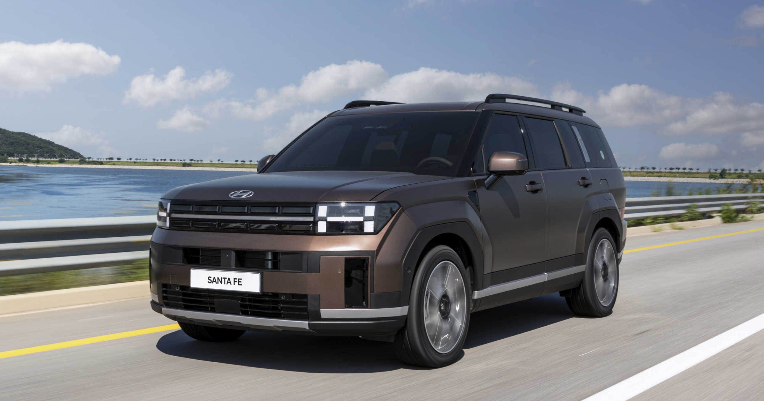 검붉은색 싼타페가 물가를 배경으로 주행하는 전측면 모습