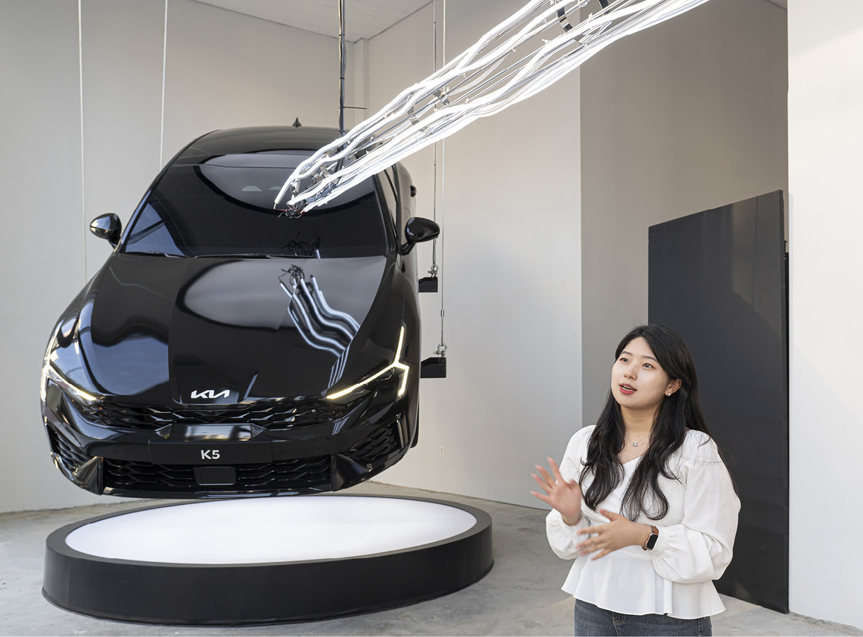 공중에 매달린 더 뉴 K5 옆에서 여성이 설명하는 모습