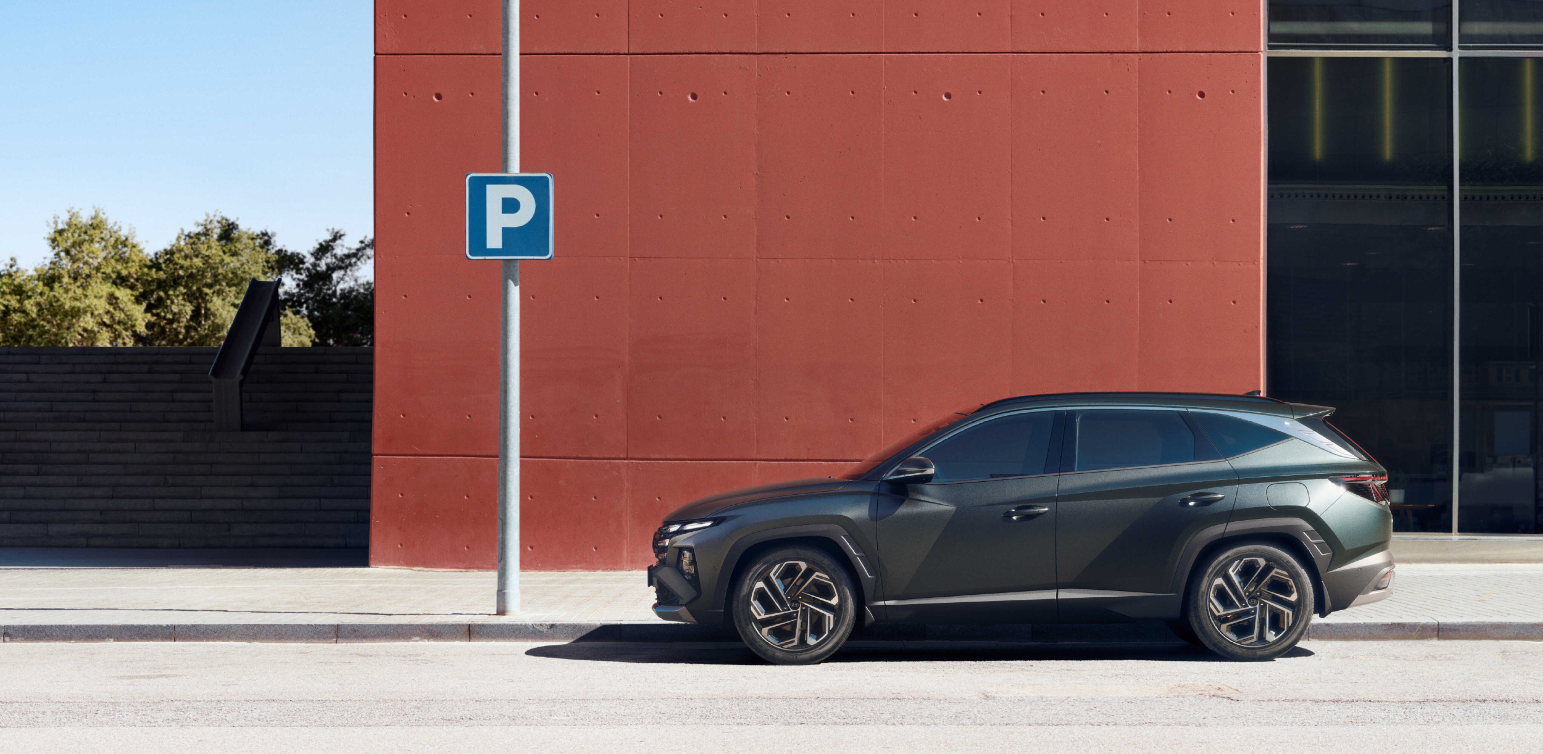 주황색으로 칠해진 건물을 배경으로 서 있는 더 뉴 투싼의 측면 모습