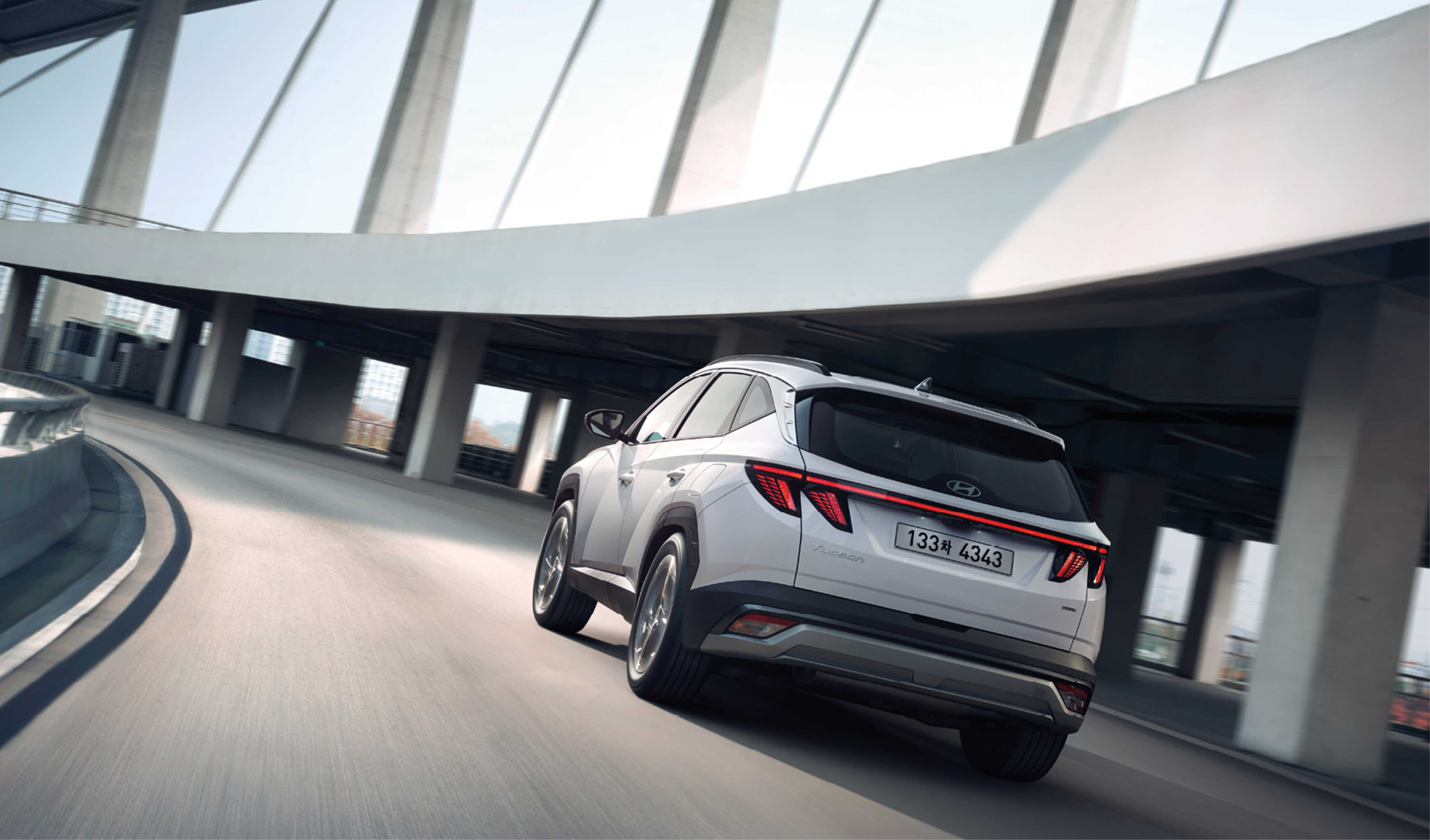 곡선 구간의 도로를 달리고 있는 더 뉴 투싼의 뒷모습