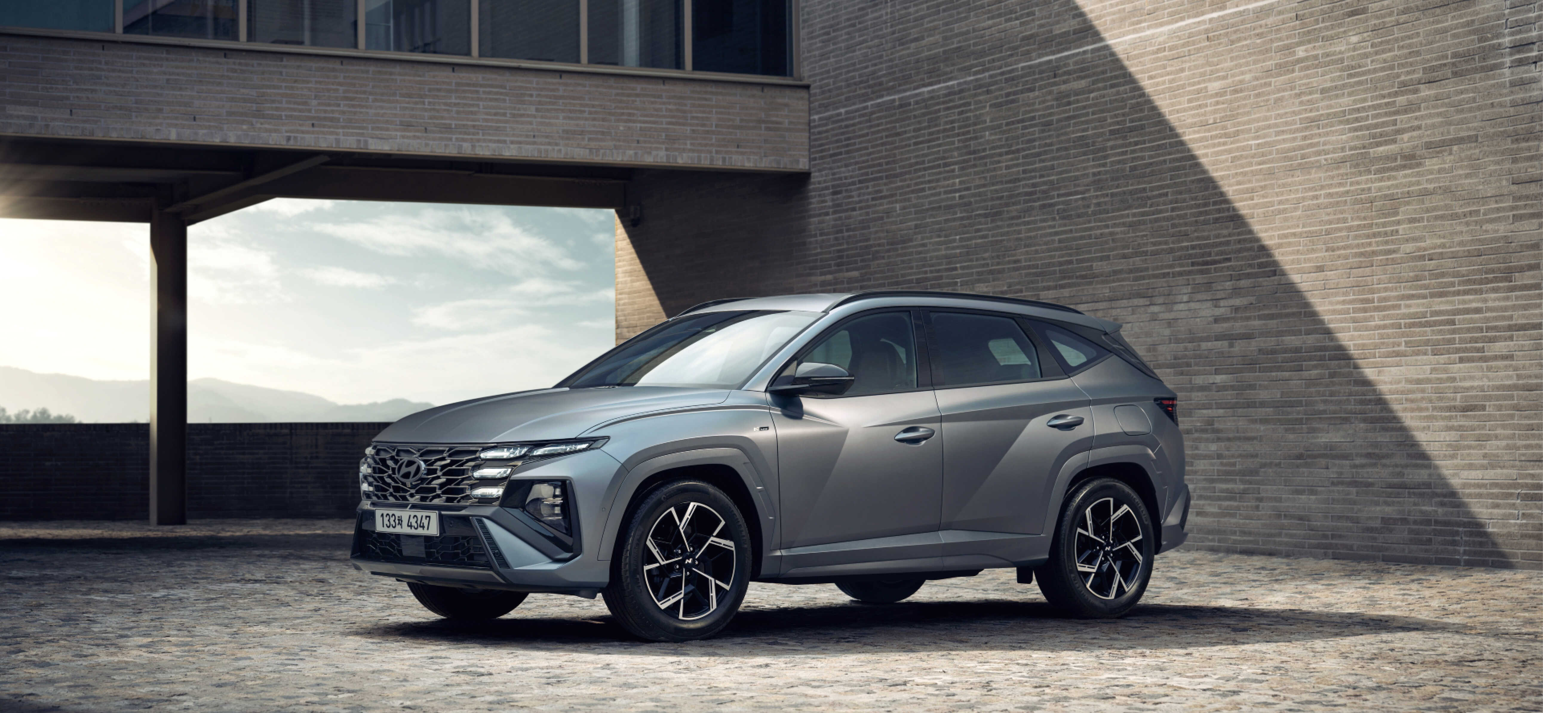 회색빛 건물을 배경으로 서 있는 더 뉴 투싼 N 라인의 전측면 모습