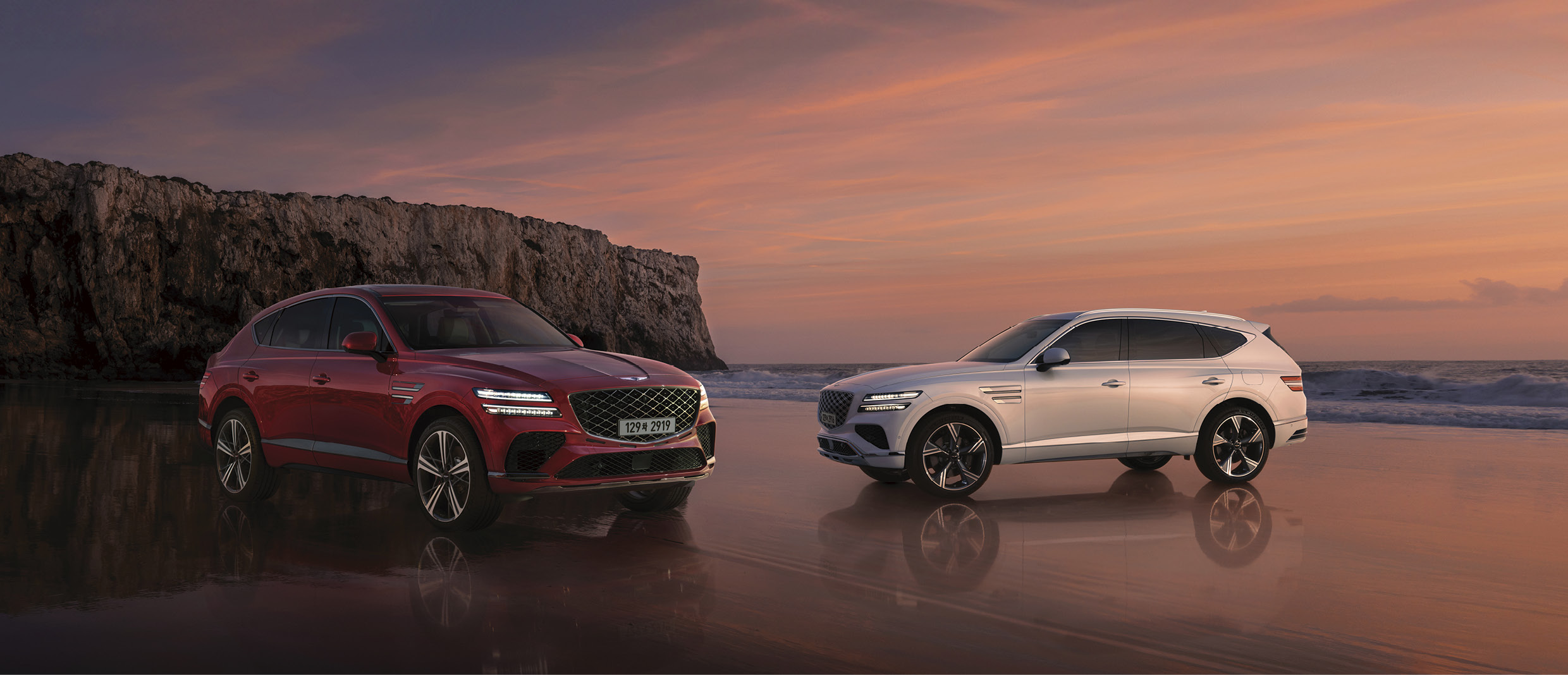 빨간색 GV80 쿠페와 흰색 GV80이 마주본 채 노을진 해변에 정차한 모습