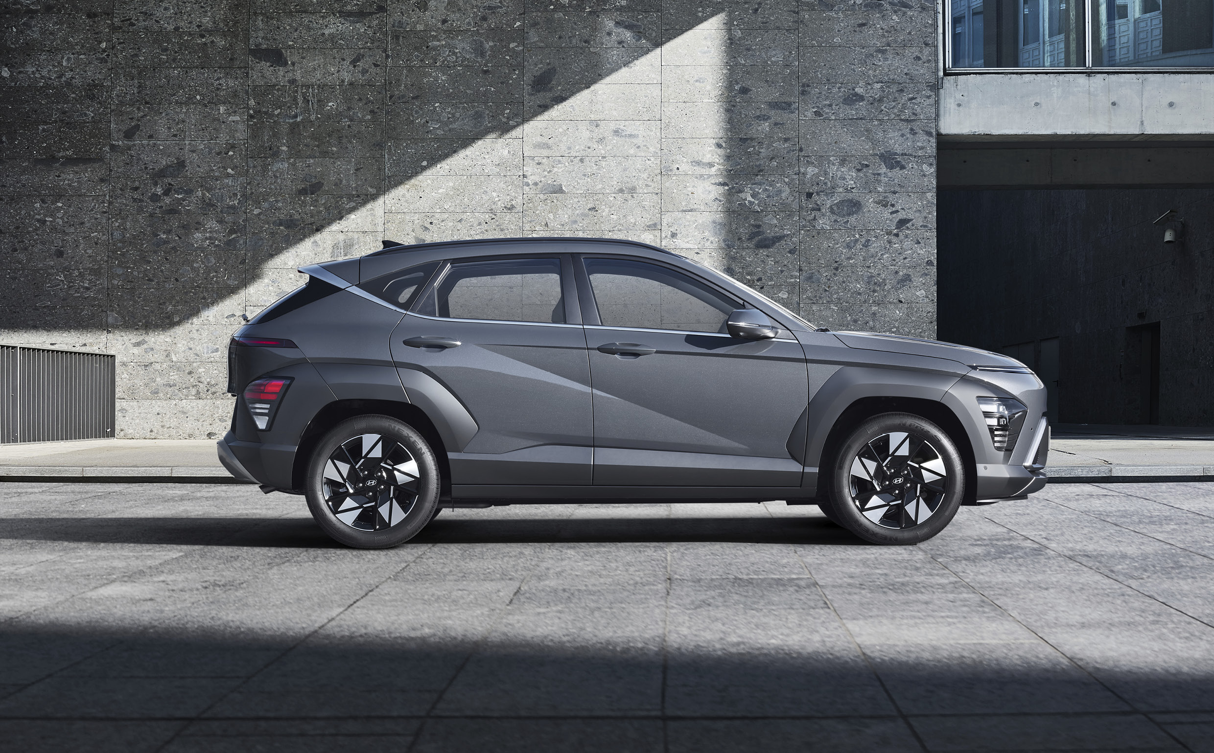 코나가 회색 건물 주변에 정차한 정측면 모습