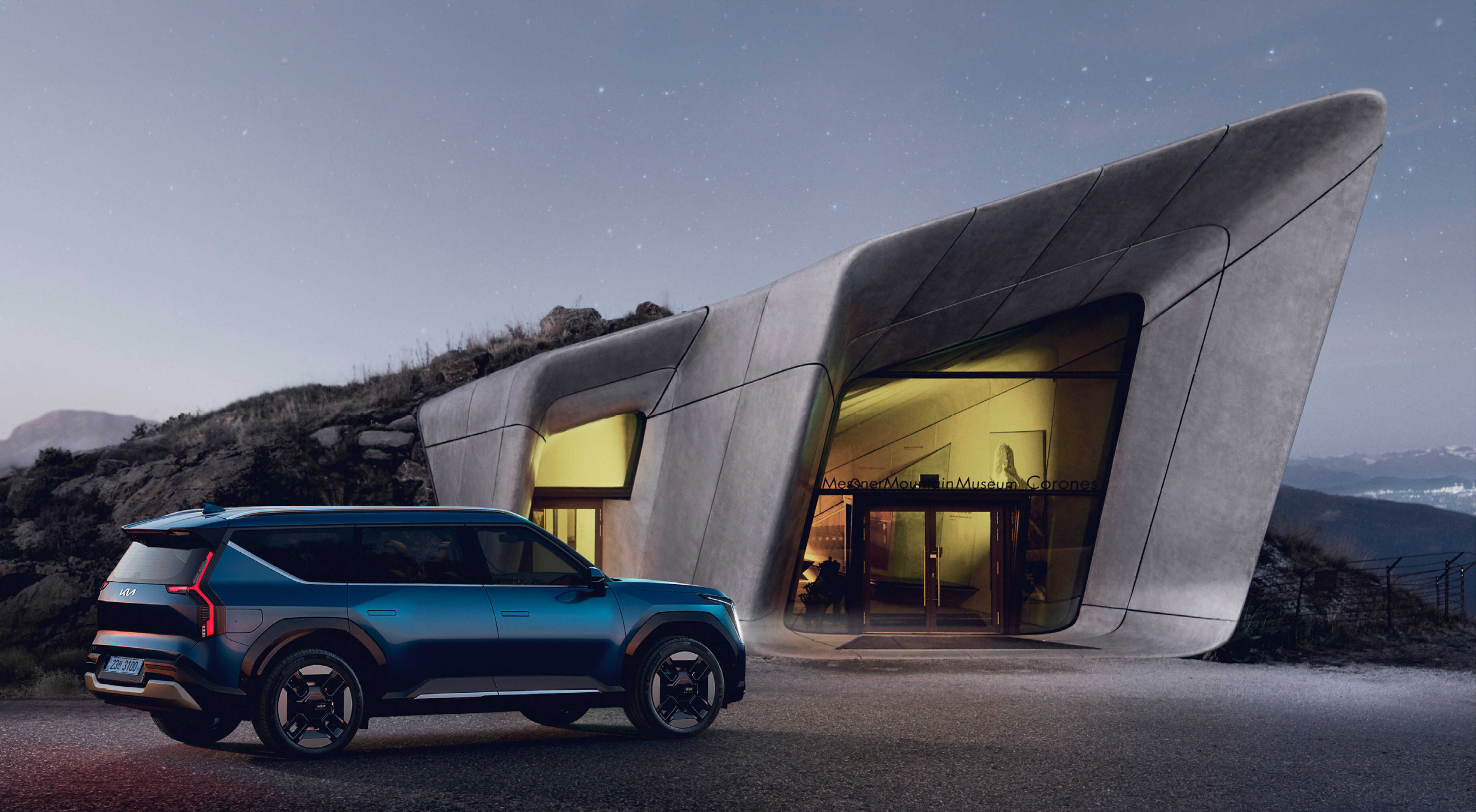 EV9's rear profile, standing in front of an unconventional building