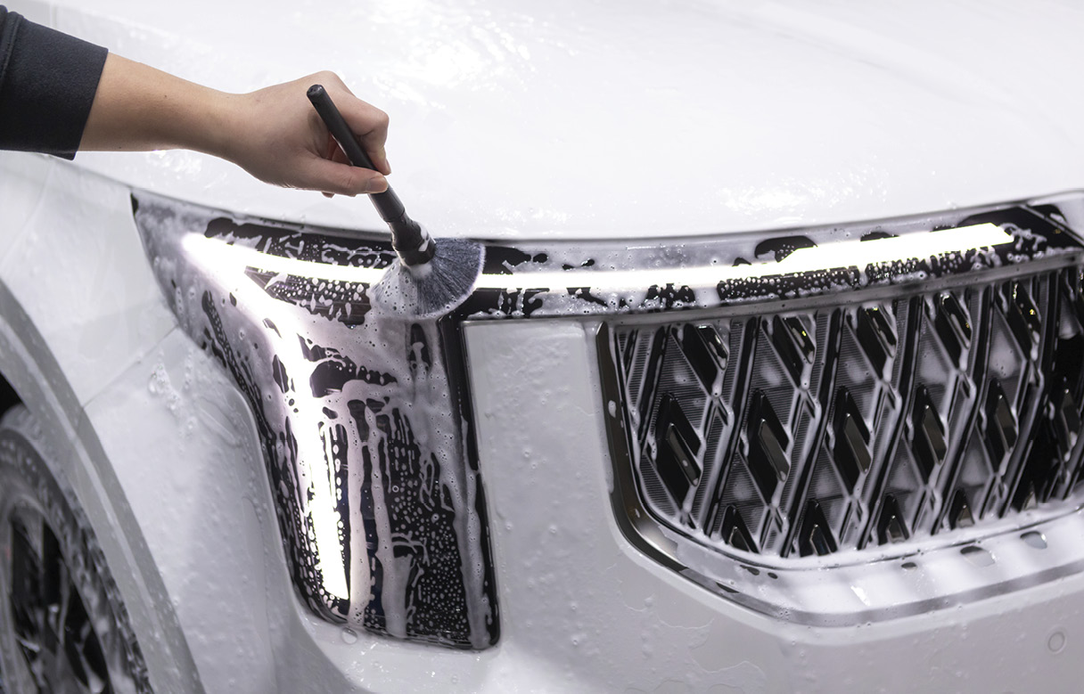 A person is cleaning the headlights of a carnival with a detailing brush