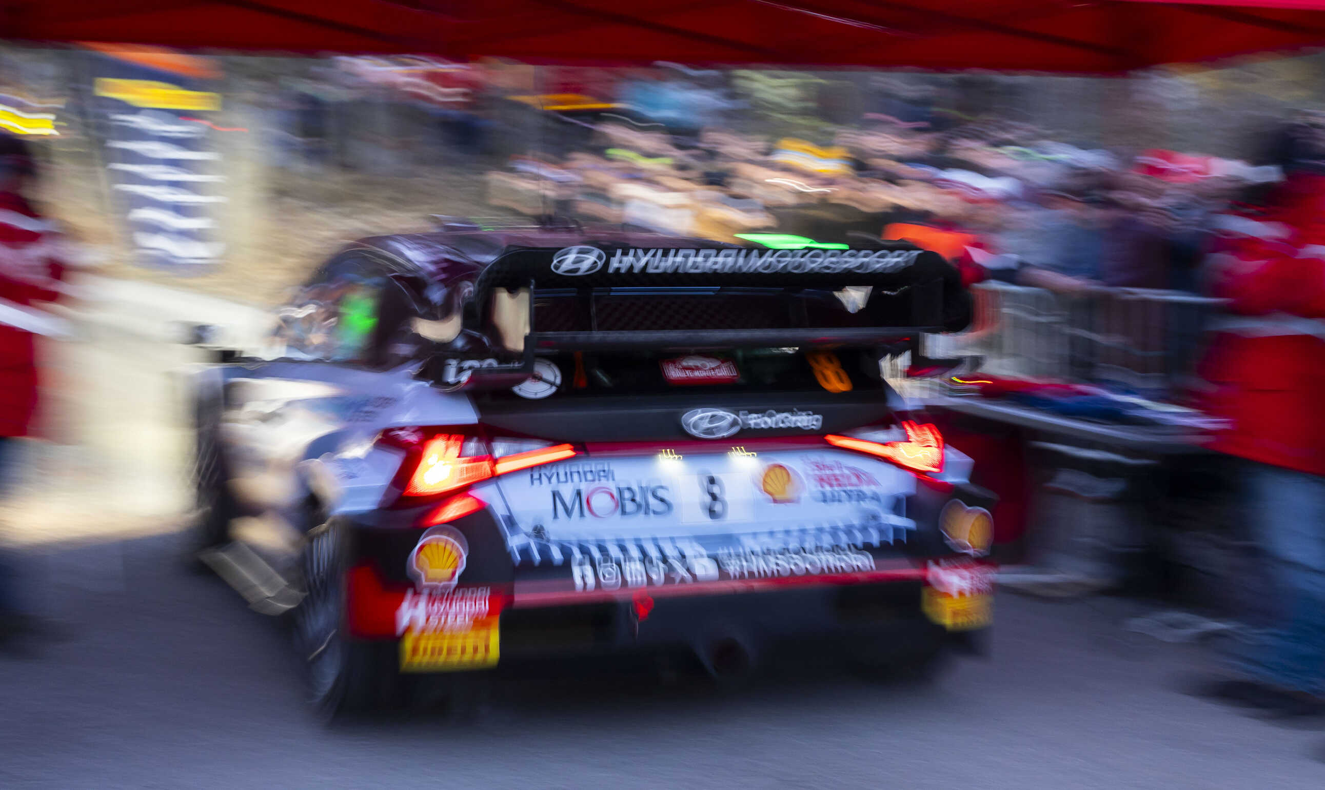 Rear/side view of Hyundai rally car departing under a red tent