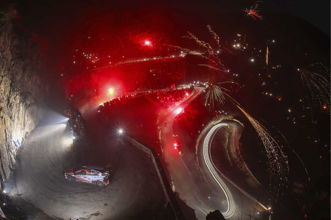 A bird's-eye view of a Hyundai rally car navigating through a series of hairpin turns on a cliff.