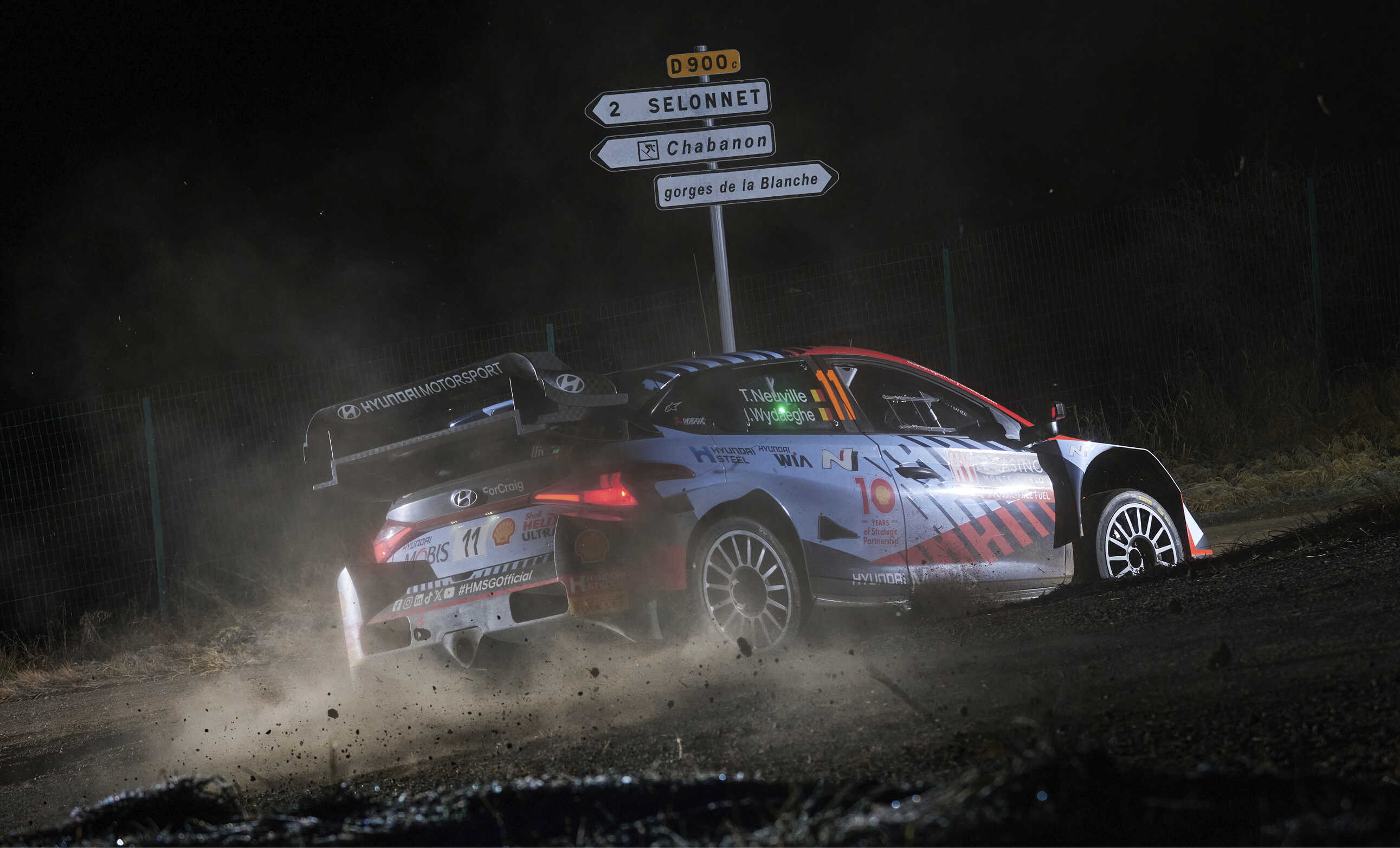 Rear/side view of a Hyundai rally car driving fast on a dark dirt road