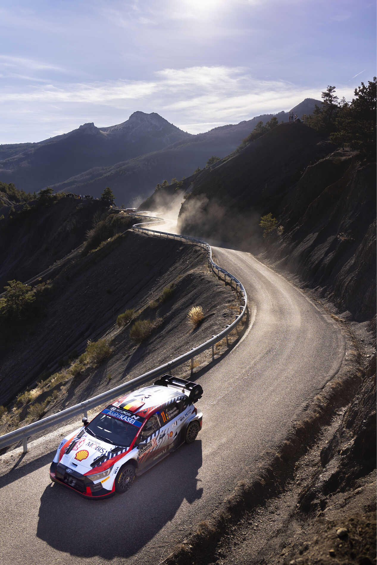A Hyundai rally car driving quickly on a winding paved road in the mountains.