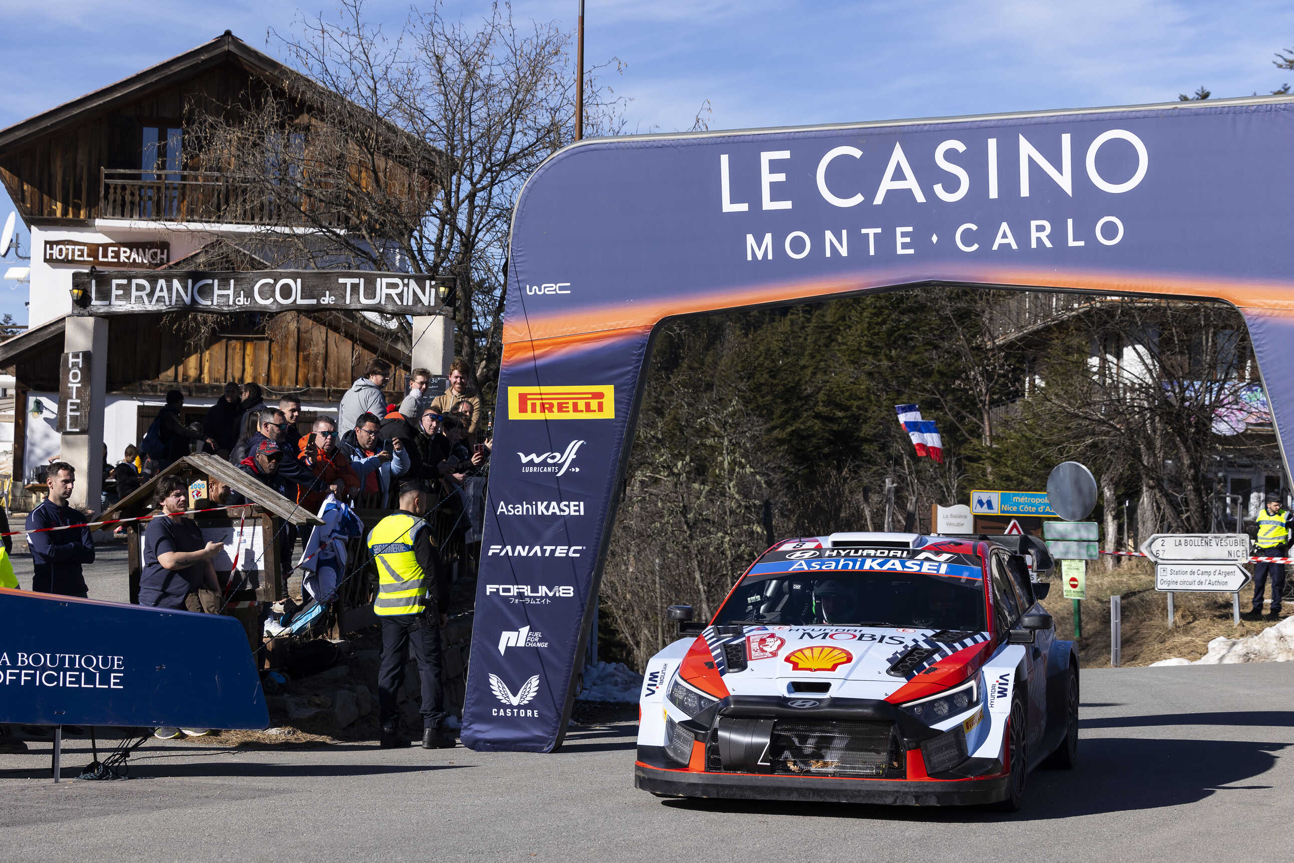 Front/side views of a Hyundai rally car speeding through a set placed on the pavement.