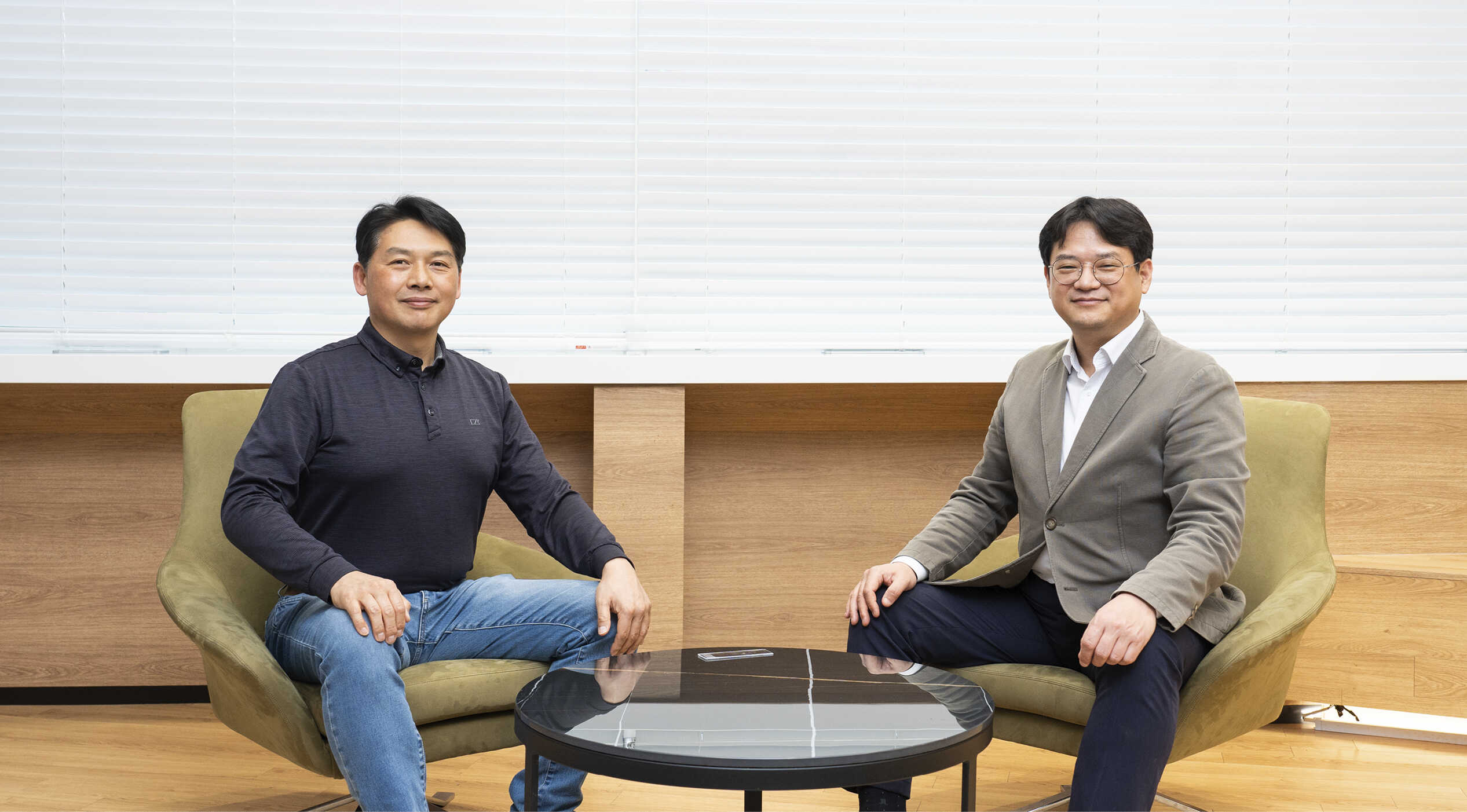 성인 남성 두 명이 독립된 의자에 앉아 정면을 향해 포즈를 취한 모습