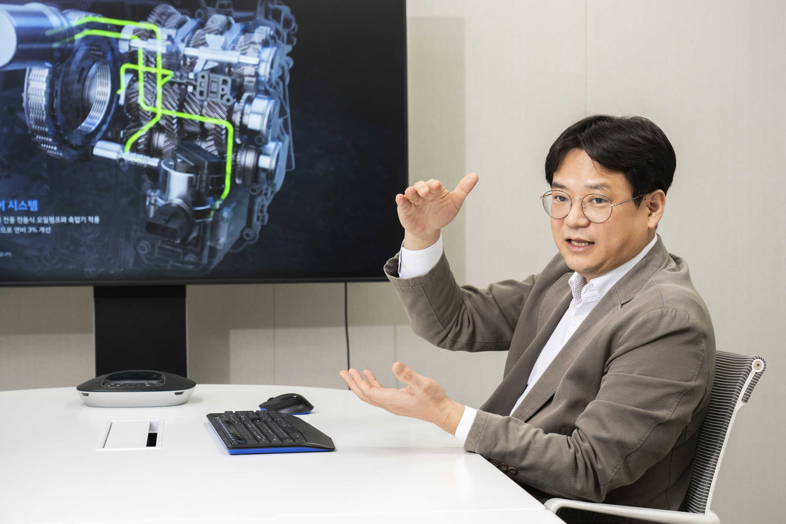 성인 남성이 TV 옆 의자에 앉아 양손을 들고 설명하는 모습