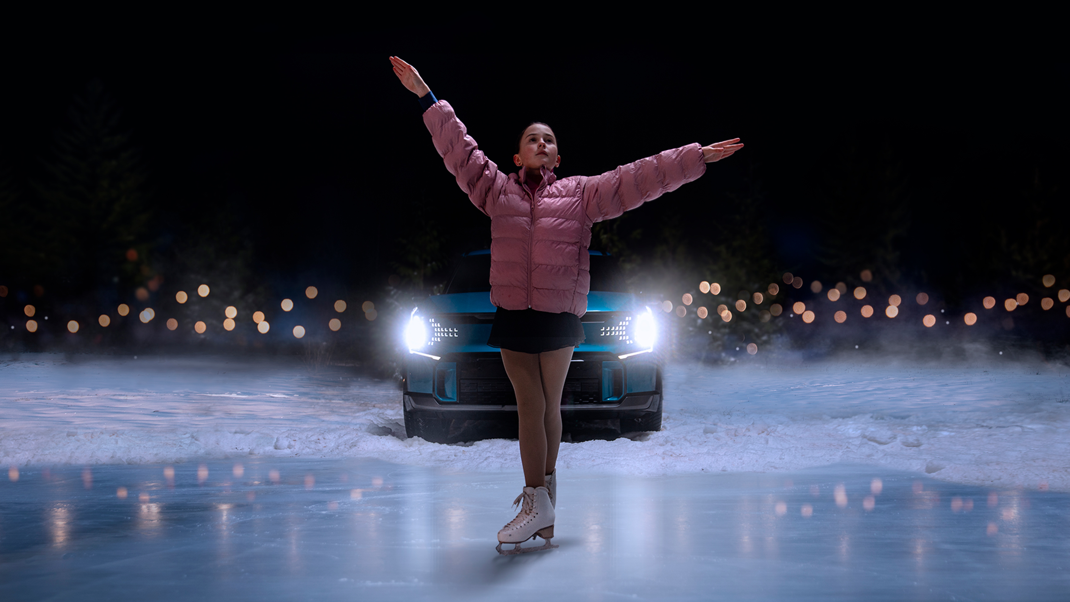 A girl spreading her arms wide and posing on the ice alongside a car.