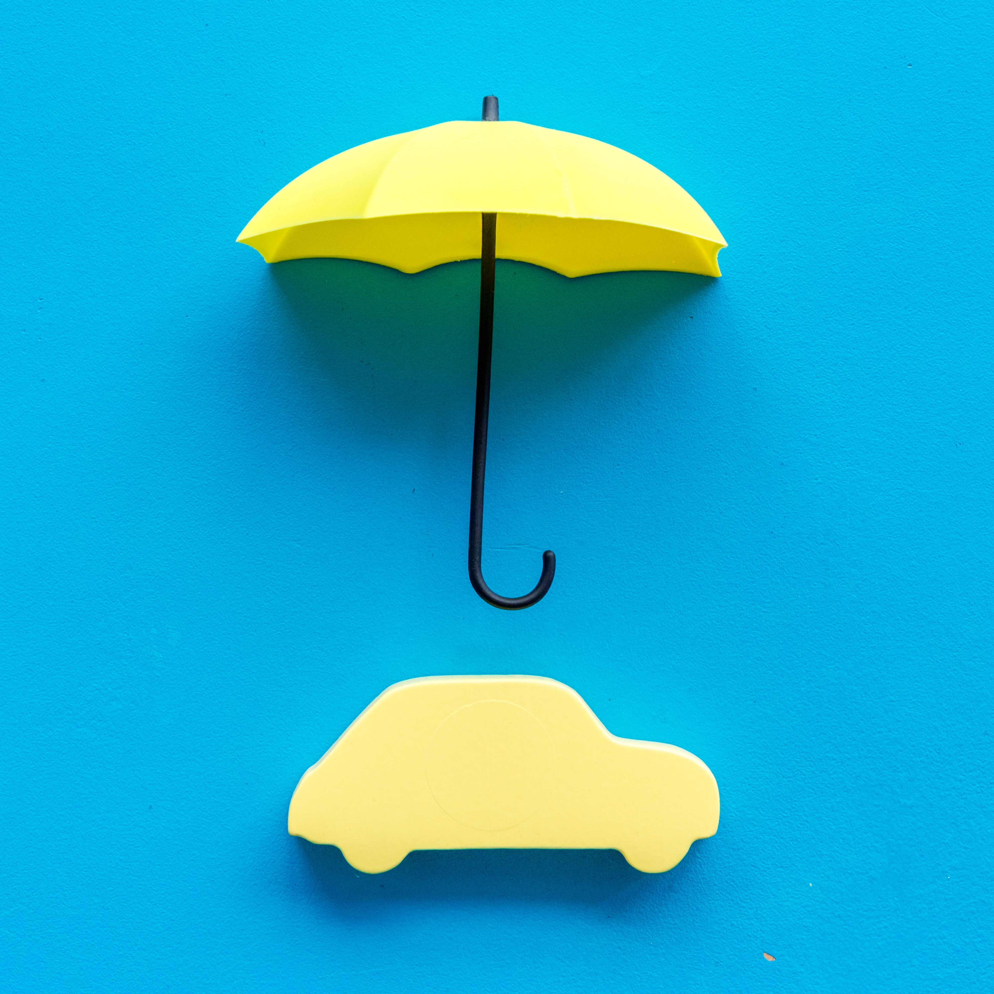 파란 배경 중심에 노란색 우산 모형과 자동차 실루엣 모형이 위 아래로 배열된 모습