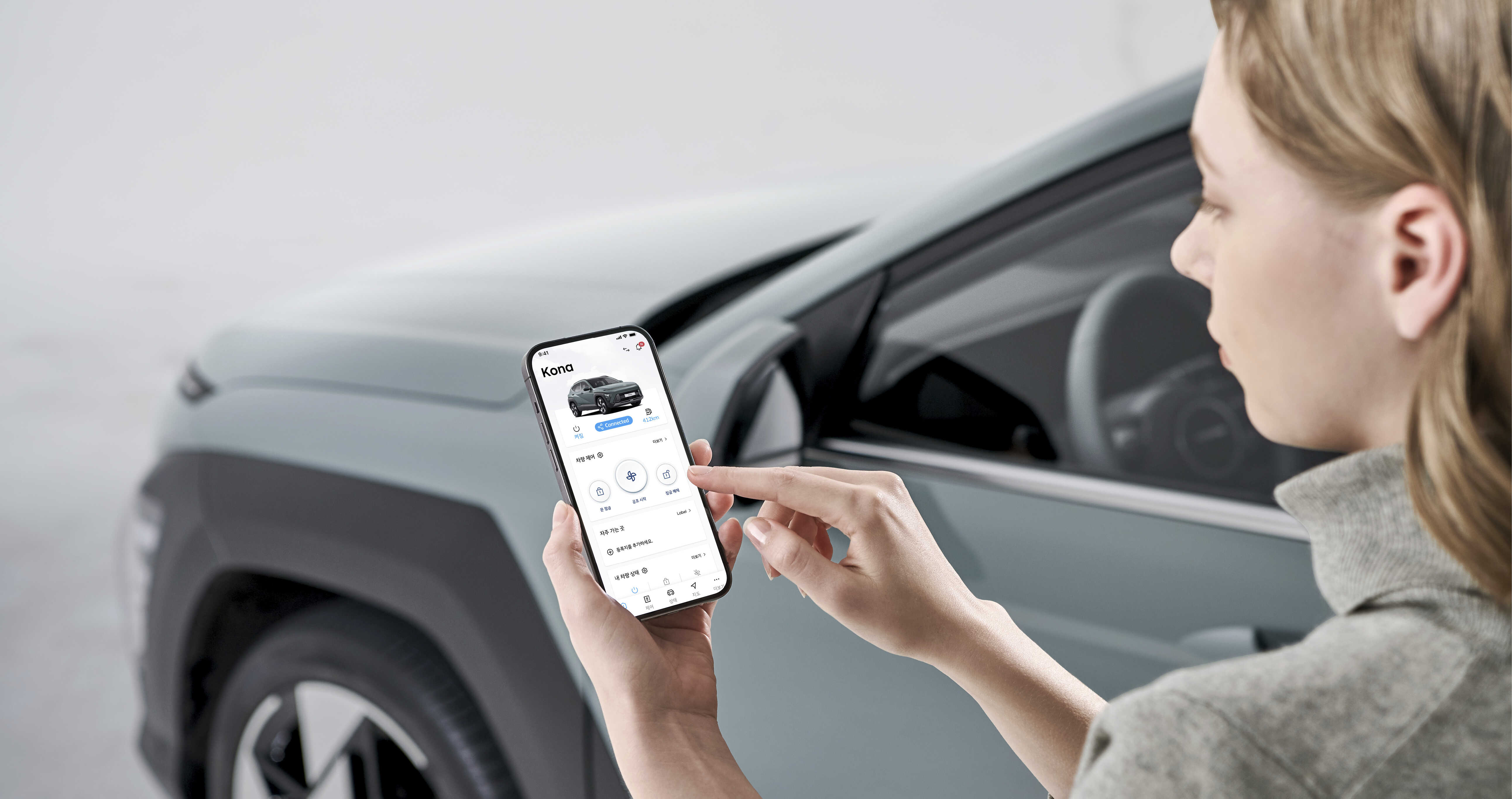스마트폰 커넥티드 서비스를 이용하는 화면과 그 배경으로 자리한 자동차 앞부분 일부 모습