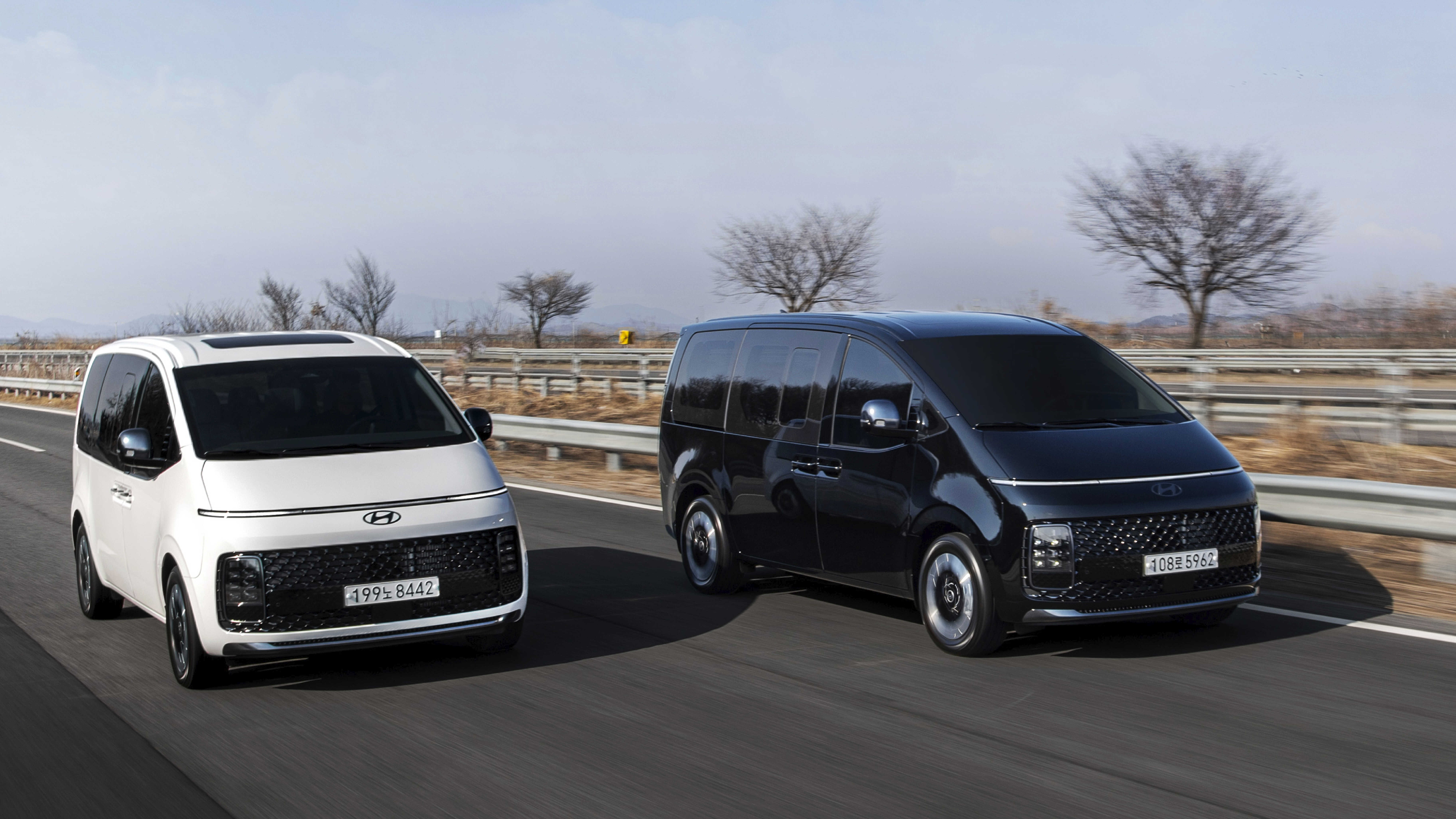 간선도로를 나란히 주행하는 흰색, 검은색 스타리아의 전측면 모습