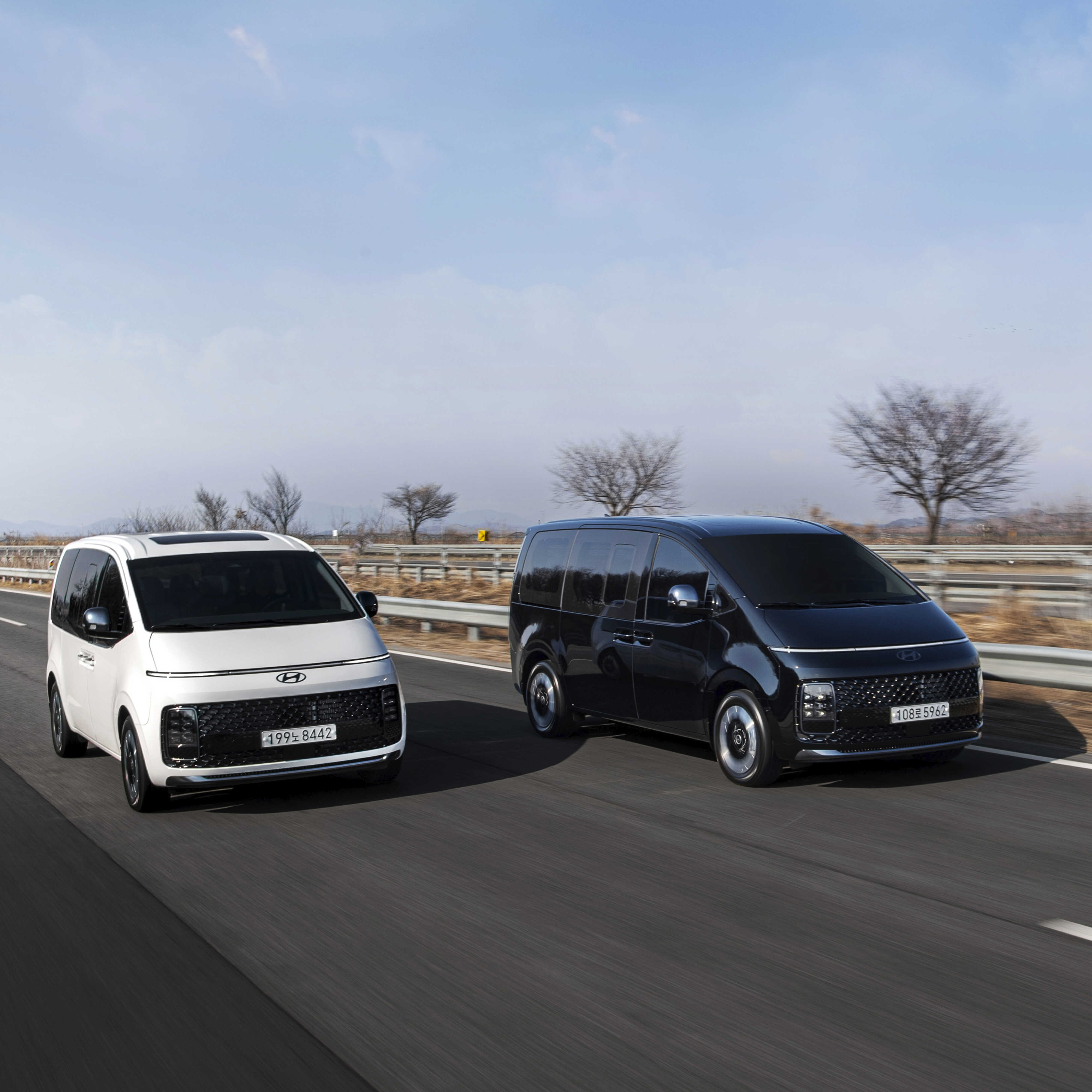 간선도로를 나란히 주행하는 흰색, 검은색 스타리아의 전측면 모습