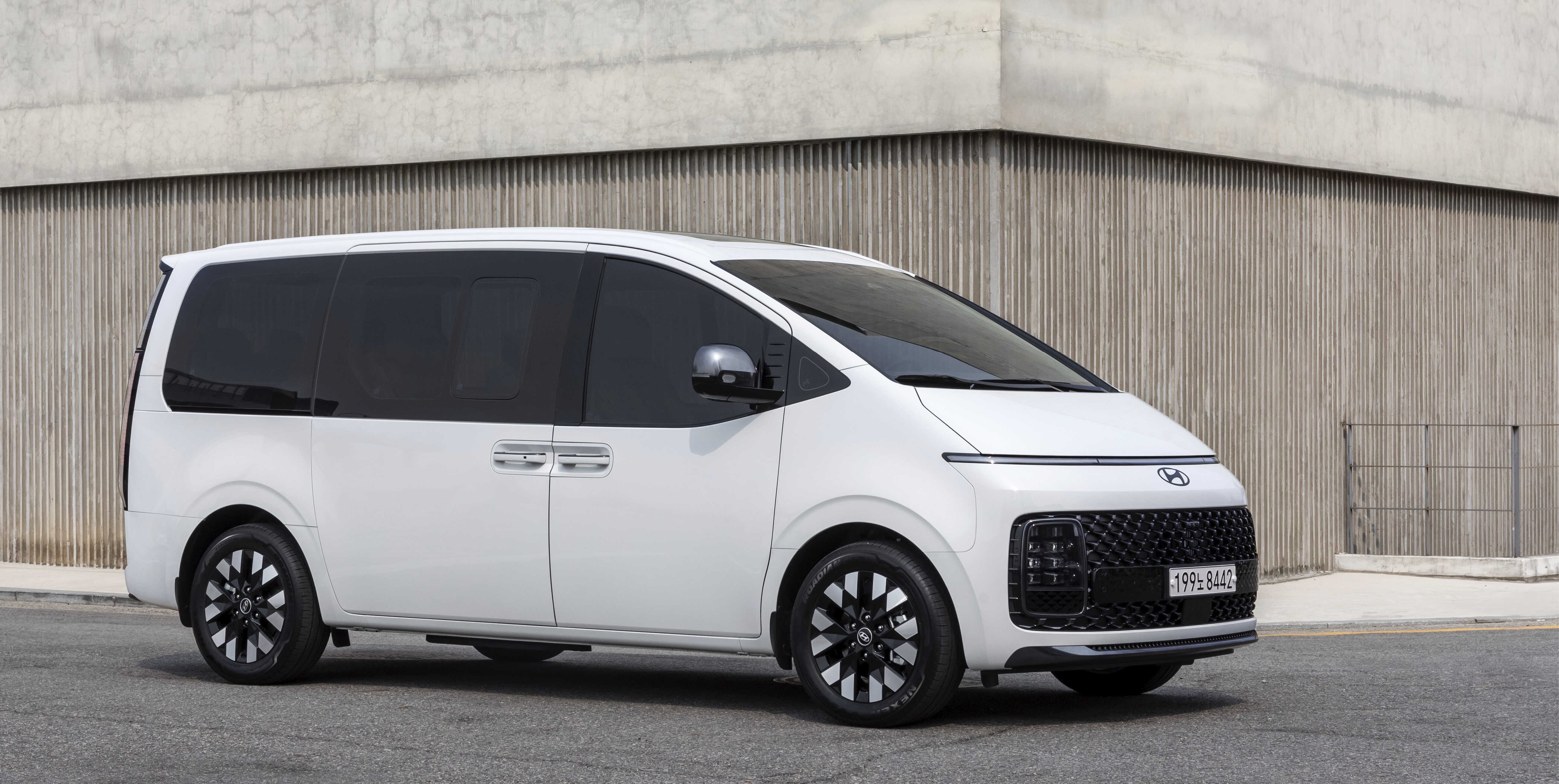 우드 장식 벽면 건물 옆에 주차된 흰색 스타리아 전측면 모습