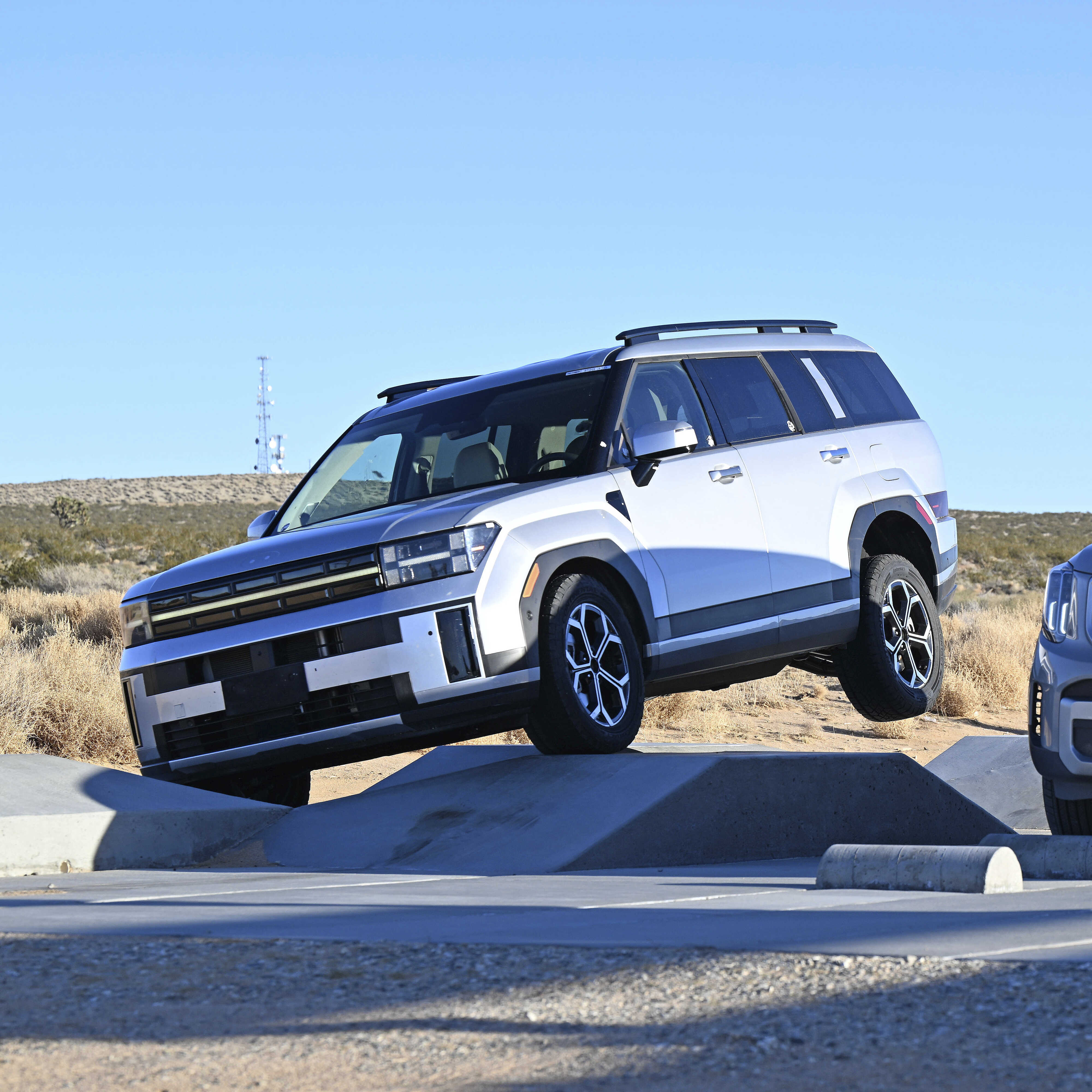 은색 SUV 두 대가 사막의 주행시험로를 나란히 주행하는 전측면 모습