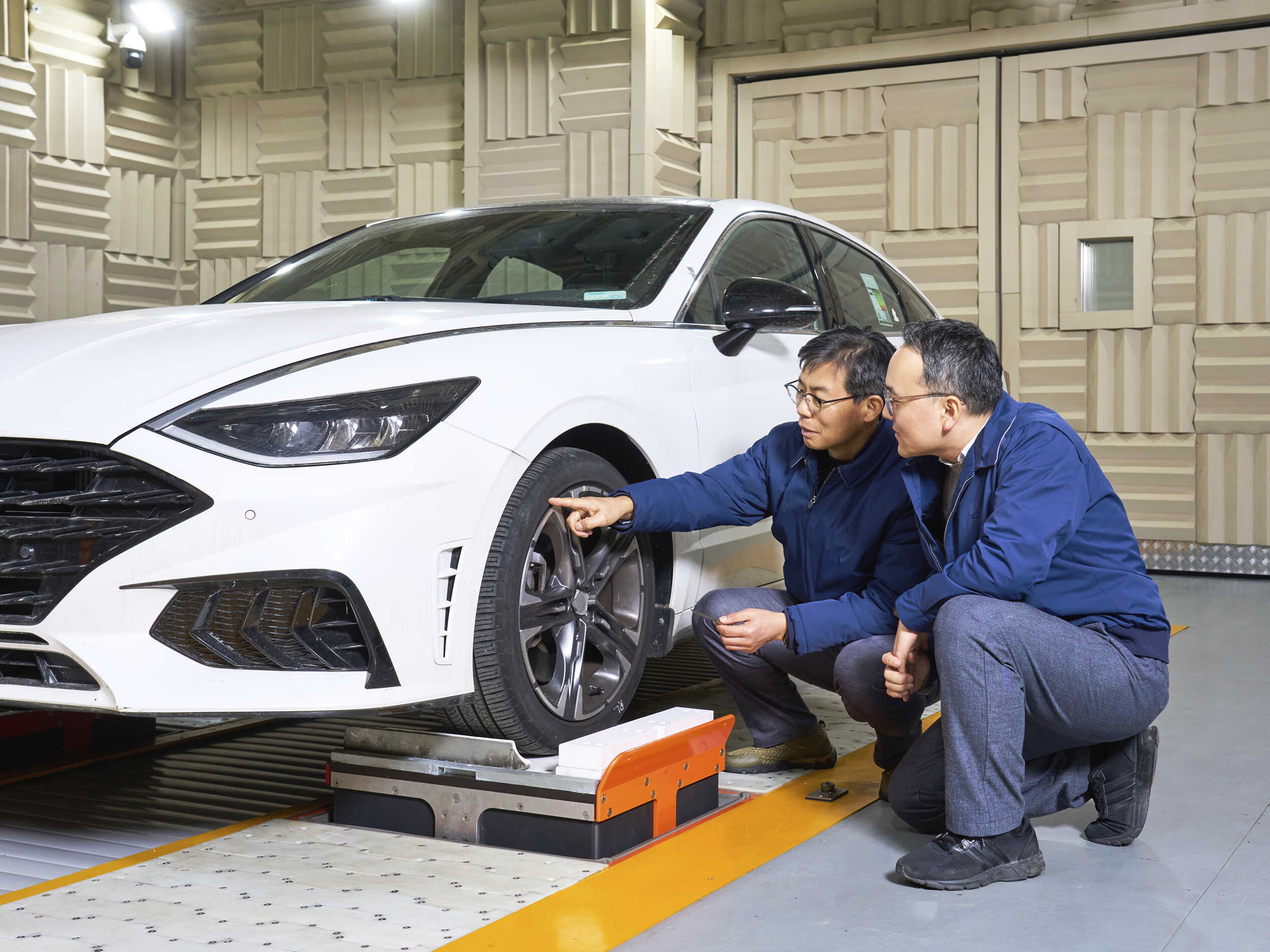 저온 챔버 시험실 내부에 흰색 승용차가 주차됐고, 운전석 앞바퀴 주변에 남성 두 명이 앉아서 이를 살피는 모습