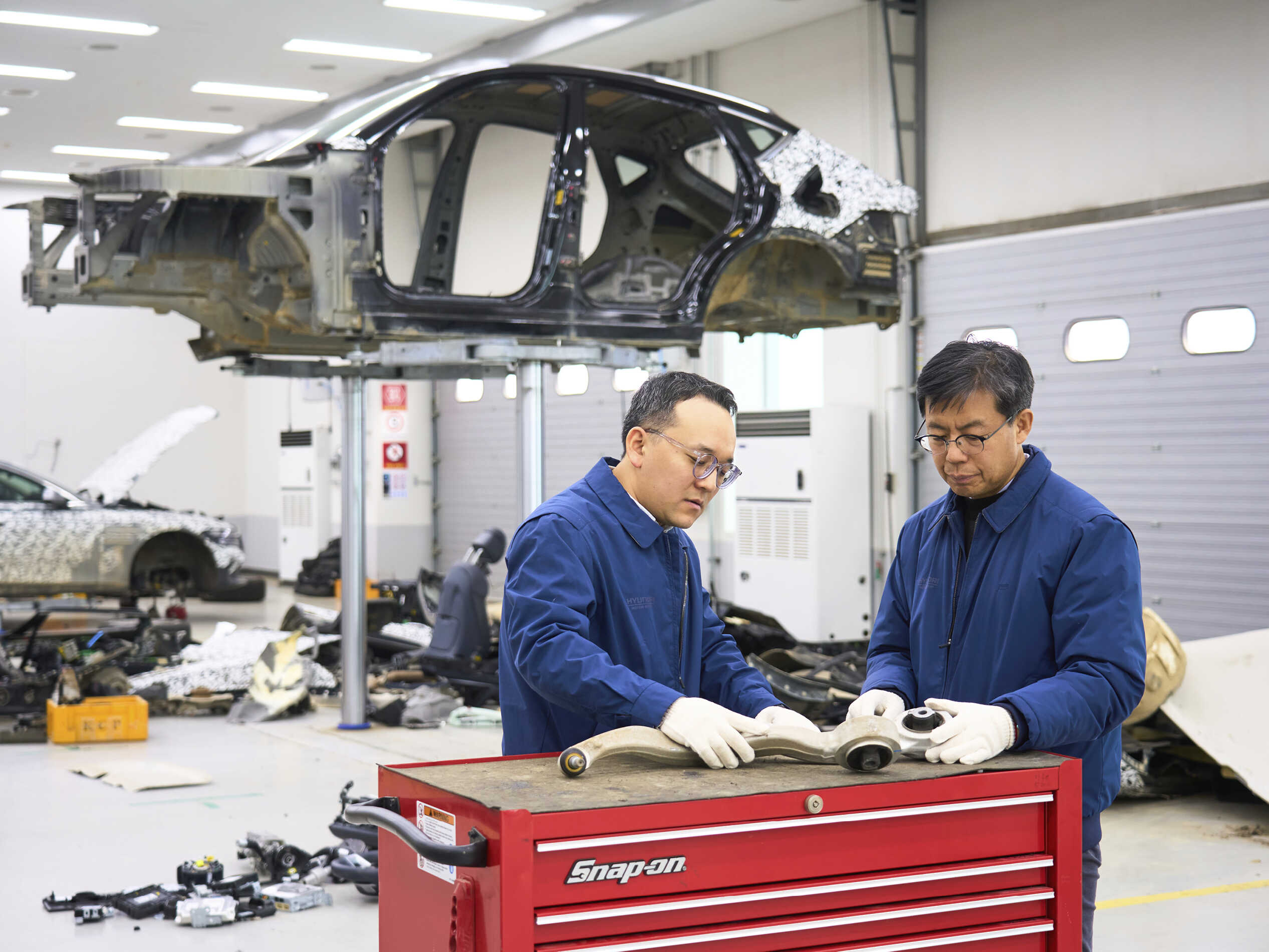 시험실 내부에 자동차가 완전히 분해됐고, 그 앞에서 분해된 부품을 살피는 남성 연구원 두 명의 모습