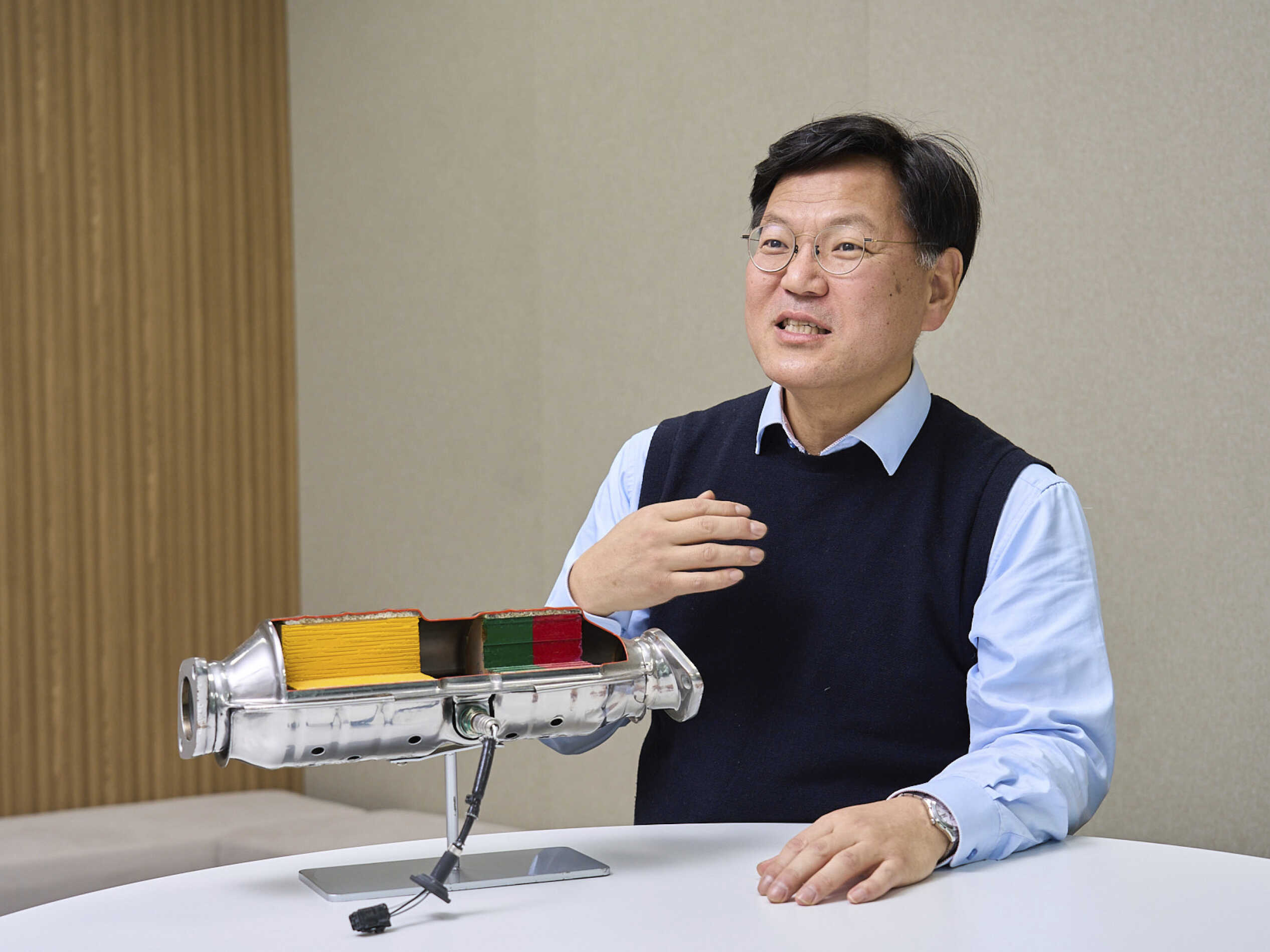 촉매 장치 절개 모형을 테이블 위에 두고 설명하는 남성의 모습