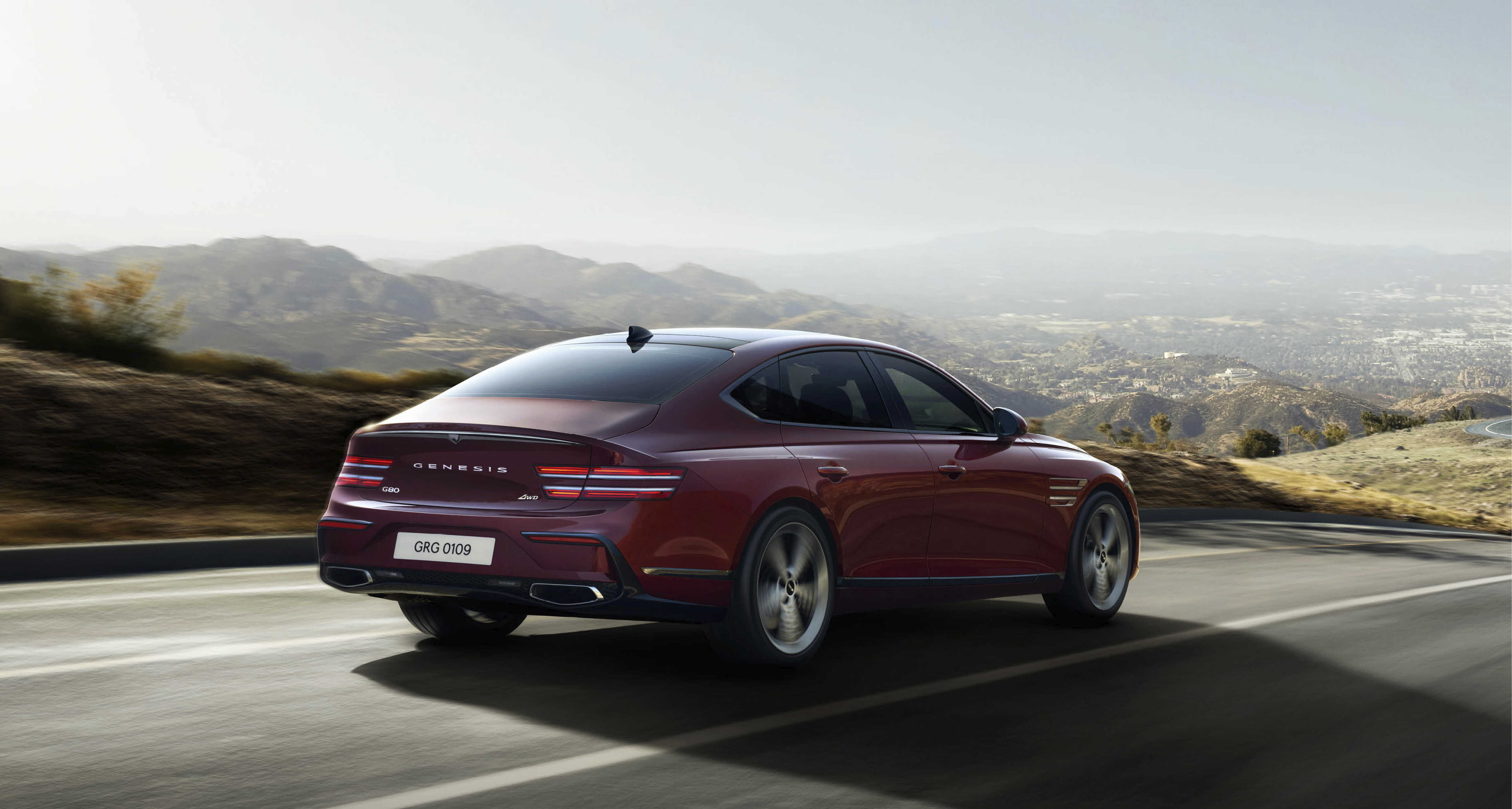 빨간색 세단이 교외 도로를 주행하는 후측면 모습