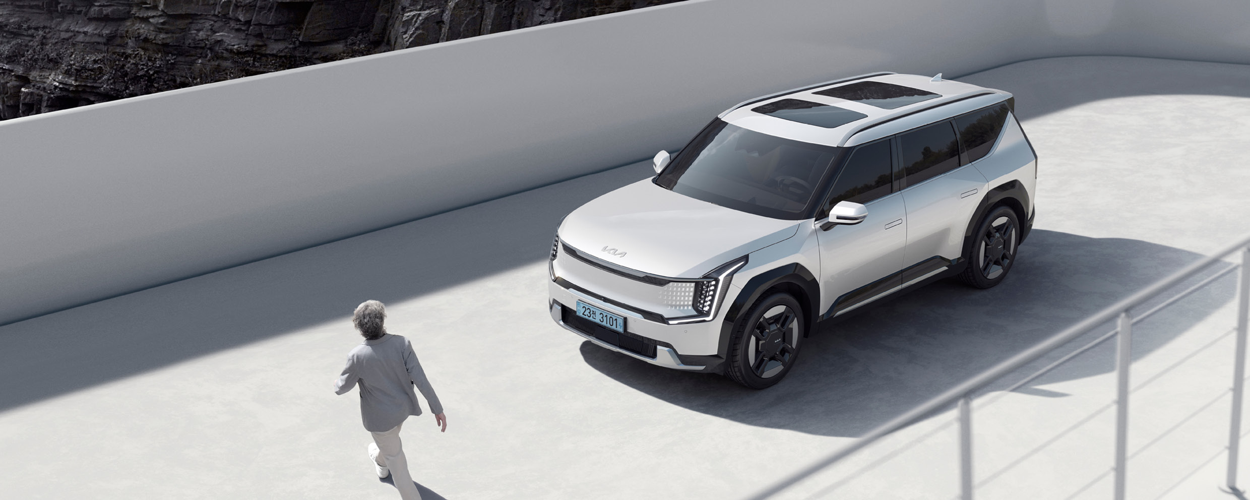 하얀색의 기아 EV9과 그 앞을 지나가는 회색 머리 남자의 모습