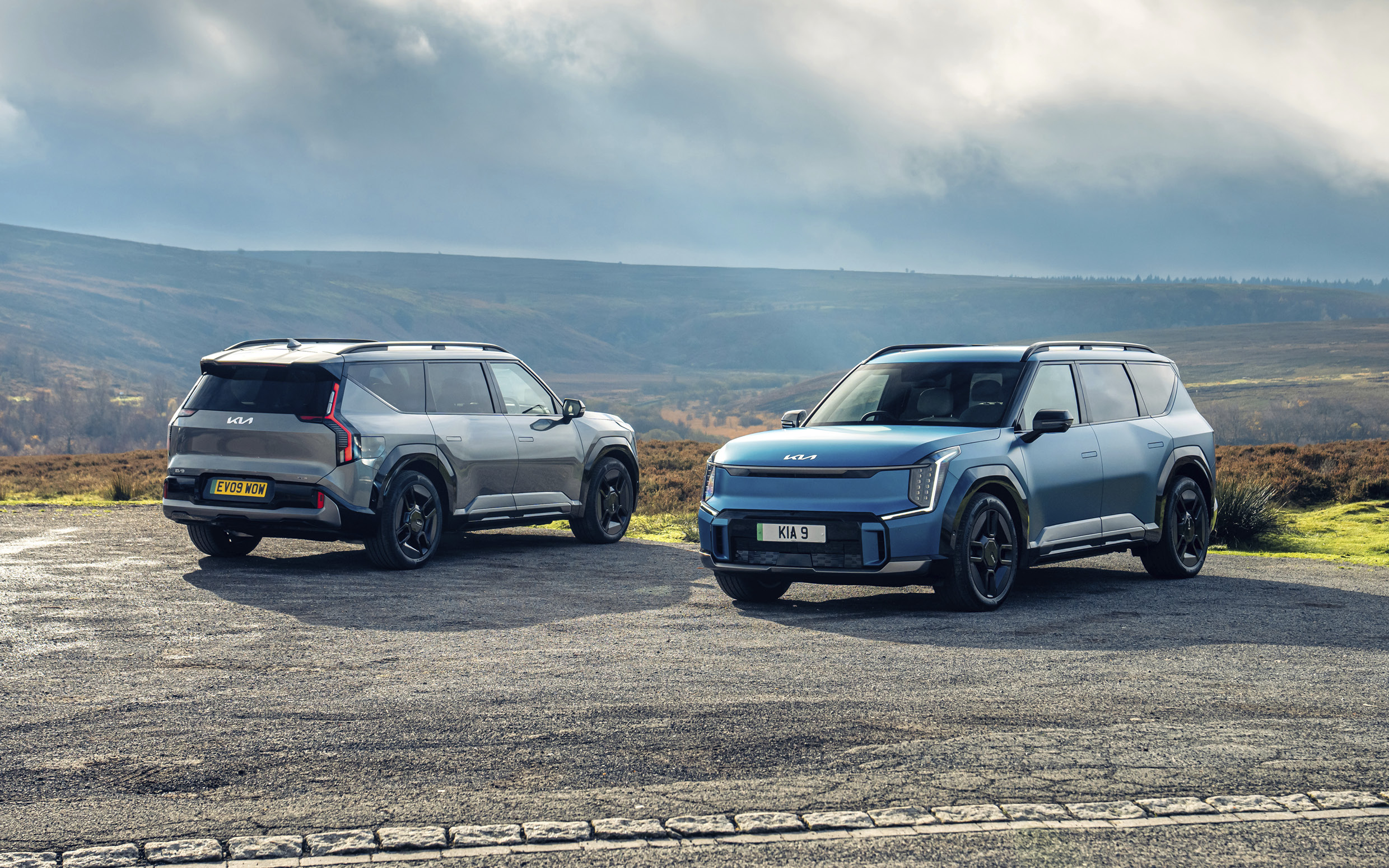 유럽 교외 지역 공터에 앞/뒤 나란히 주차된 EV9 두대의 전측면 및 후측면 모습