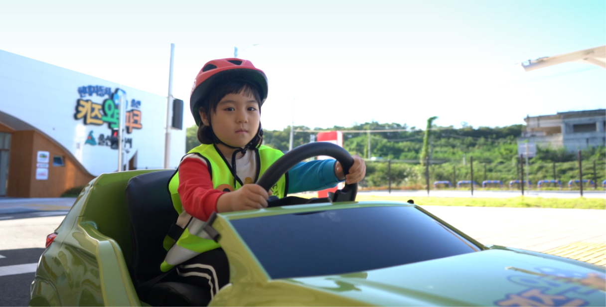 장난감 자동차 위에 헬멧을 쓰고 앉아 있는 어린이의 모습