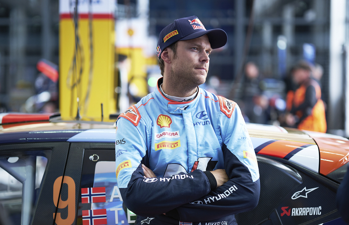Mikkelsen is posing in front of Rally cars