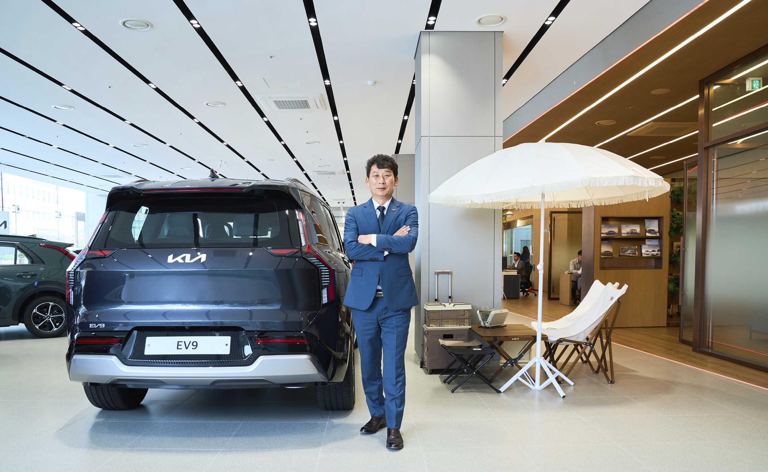 자동차 전시장 가운데 중년 남성이 팔짱을 낀채 포즈를 취한 모습
