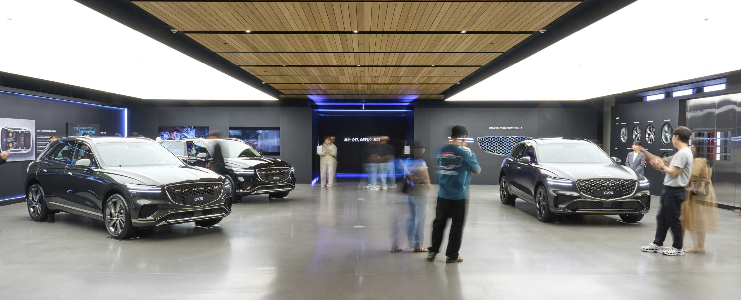 Visitors are busy moving in an indoor exhibition hall with three cars on display