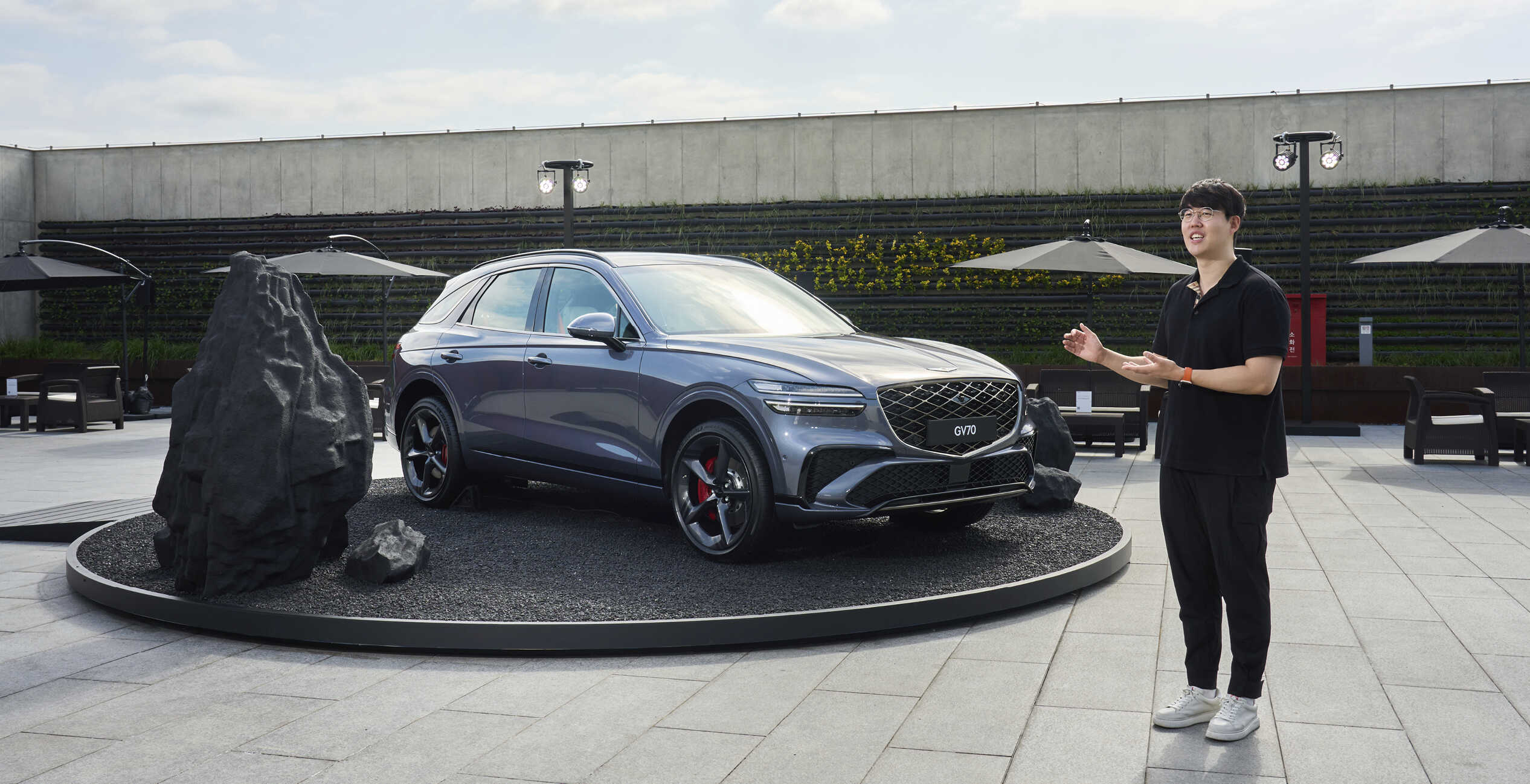 야외 무대에 전시된 그레이 중형 SUV 앞에서 남성이 설명하는 모습