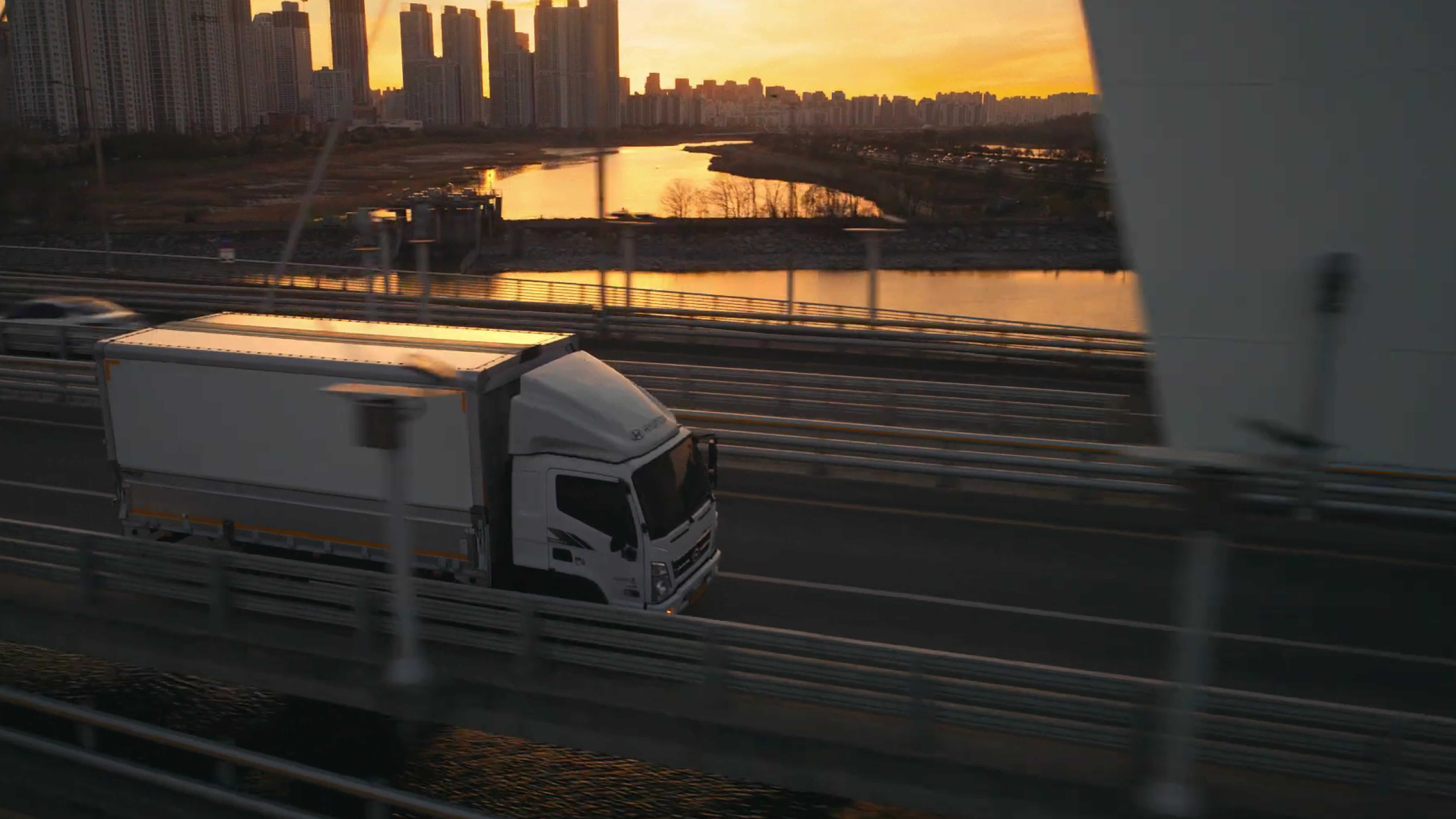 노을 배경에서 주행하는 트럭의 전측면