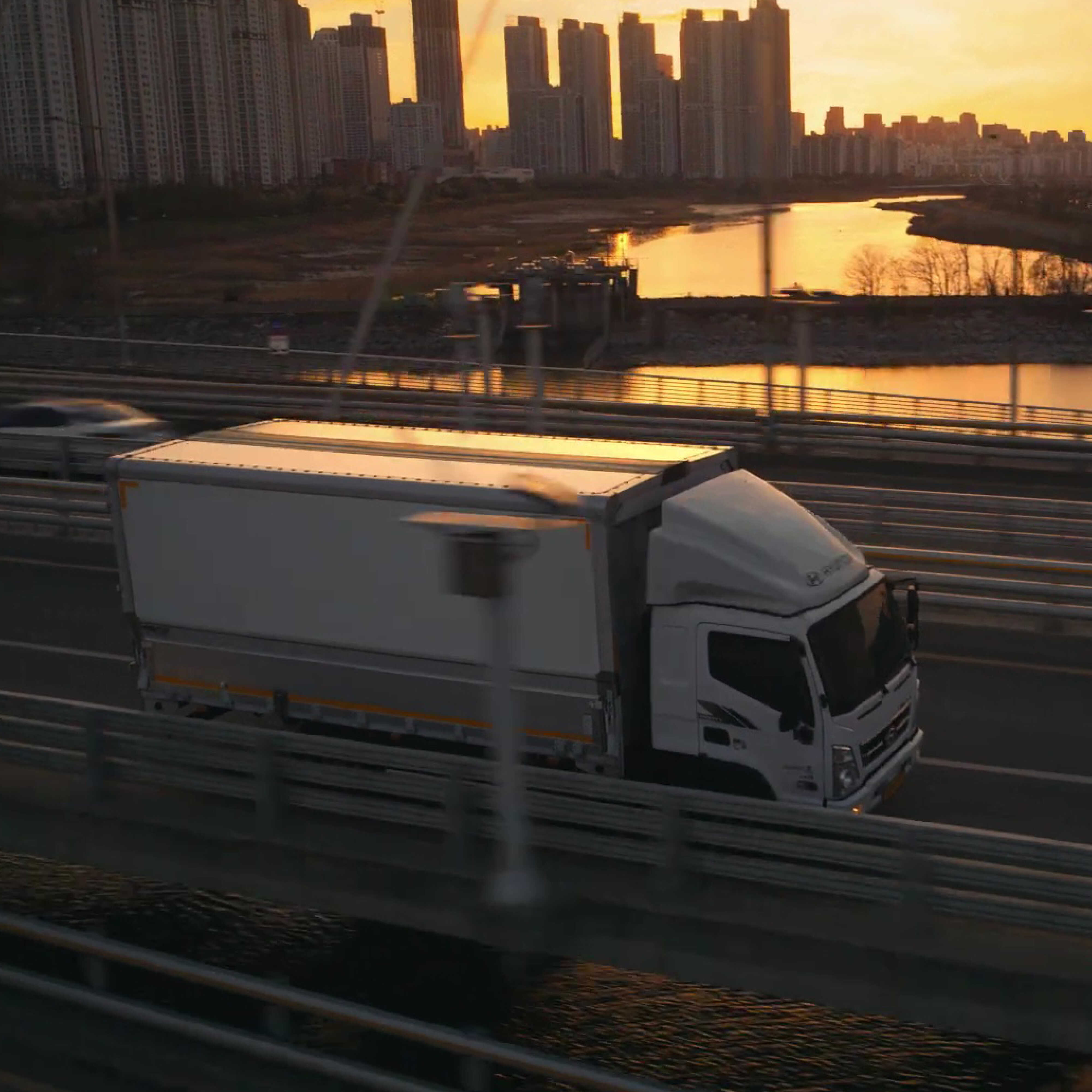 노을 배경에서 주행하는 트럭의 전측면