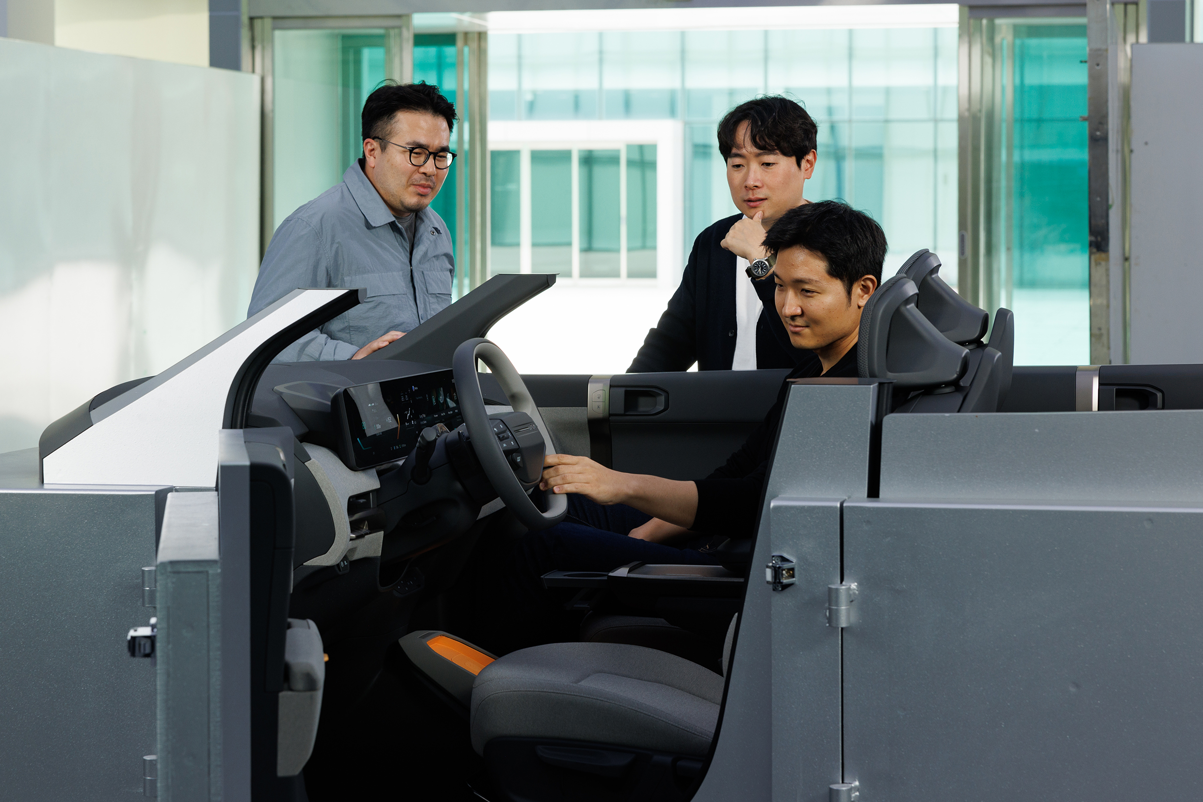 성인 남성 세 명이 디자인 개발 제품 주변에 모여 서로 이야기를 나누는 모습