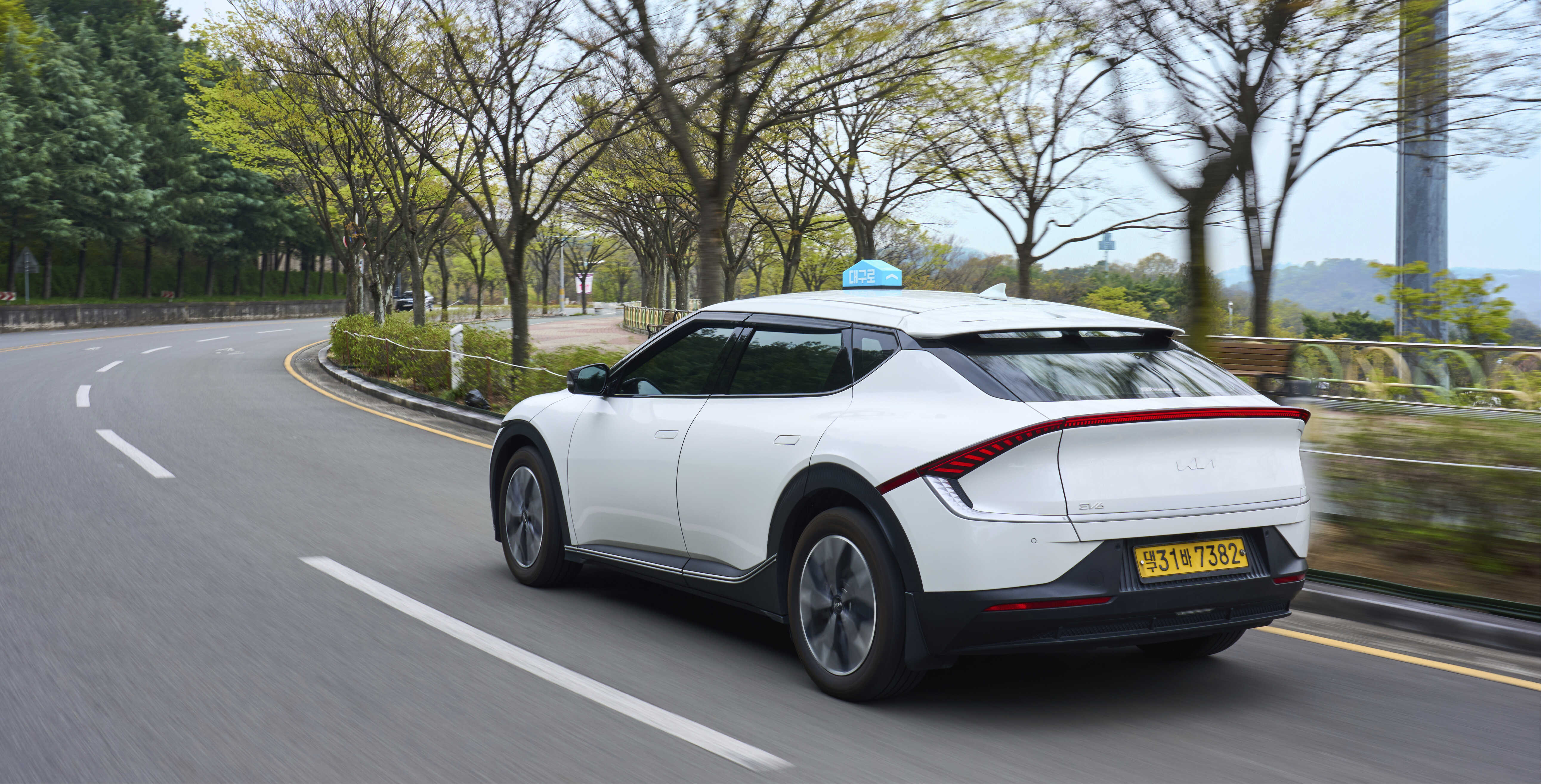 공원 도로를 주행하는 흰색 택시 후측면 모습