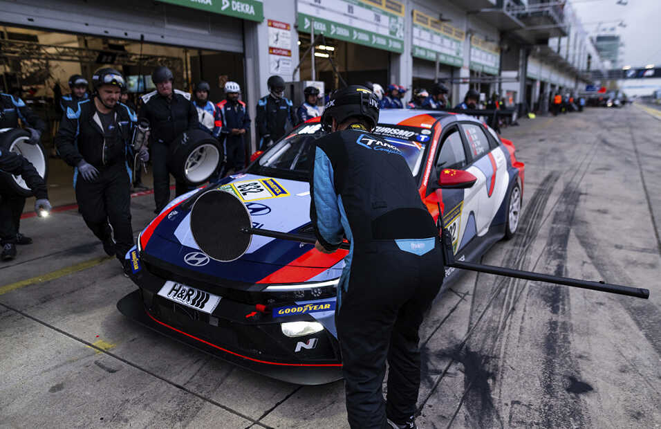 아반떼 N TCR이 피트 스탑하고, 그 주변으로 미캐닉들이 모여 타이어 교체를 진행하는 모습