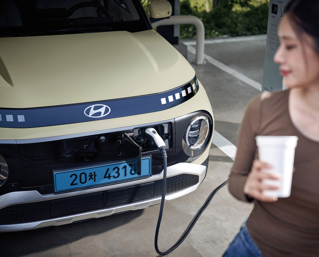 충전 중인 차량과 손에 컵을 들고 있는 여성의 모습