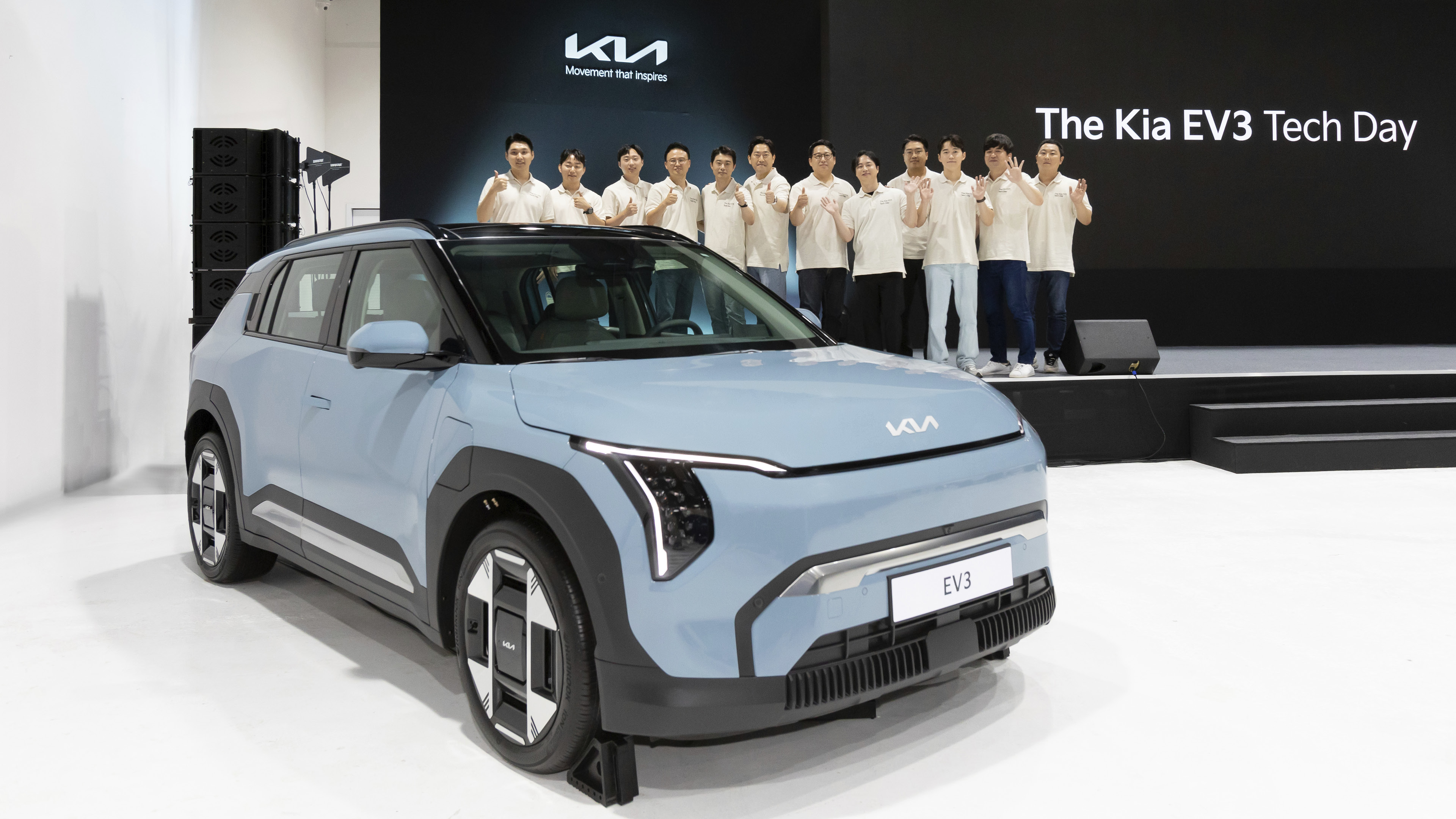 하늘색 자동차 뒤로 무대에 올라선 사람들이 포즈를 취한 모습