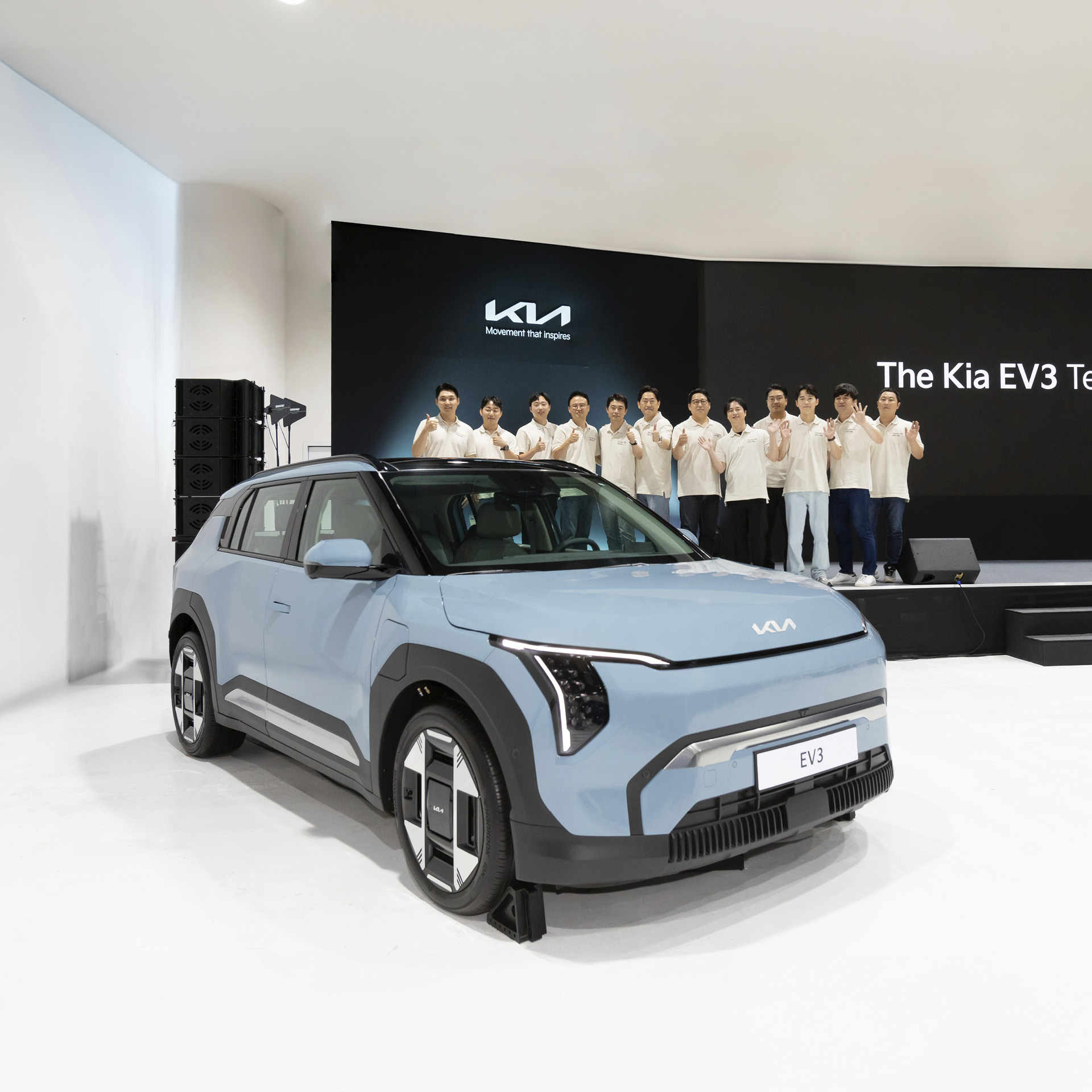 하늘색 자동차 뒤로 무대에 올라선 사람들이 포즈를 취한 모습