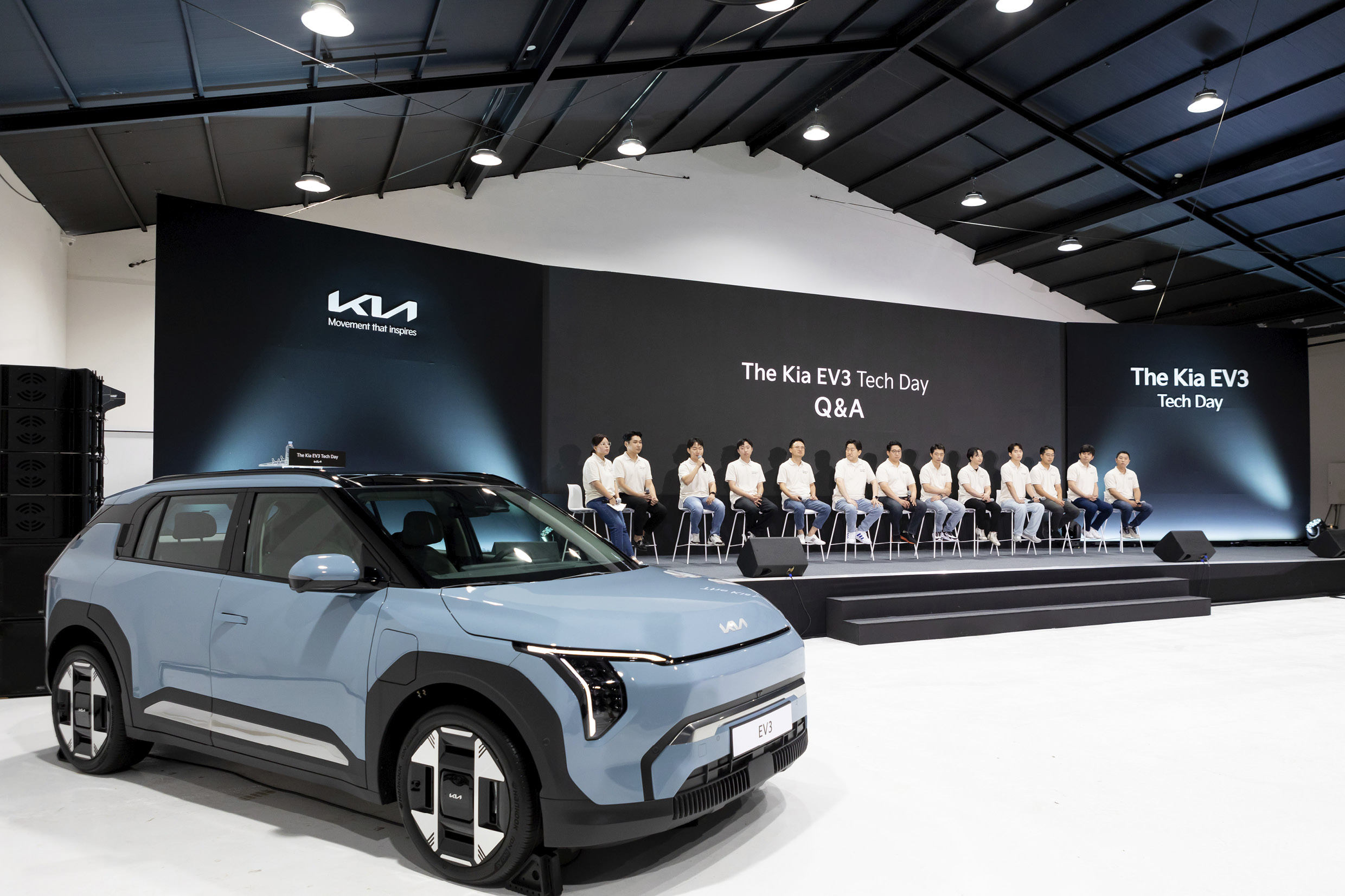 Researchers sitting on chairs on a stage behind a sky blue vehicle