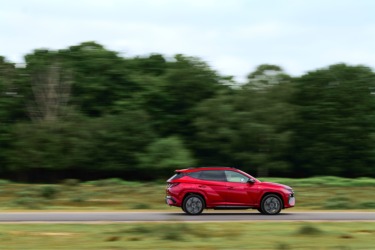 빨간색 SUV가 숲길을 빠르게 주행하는 정측면 모습
