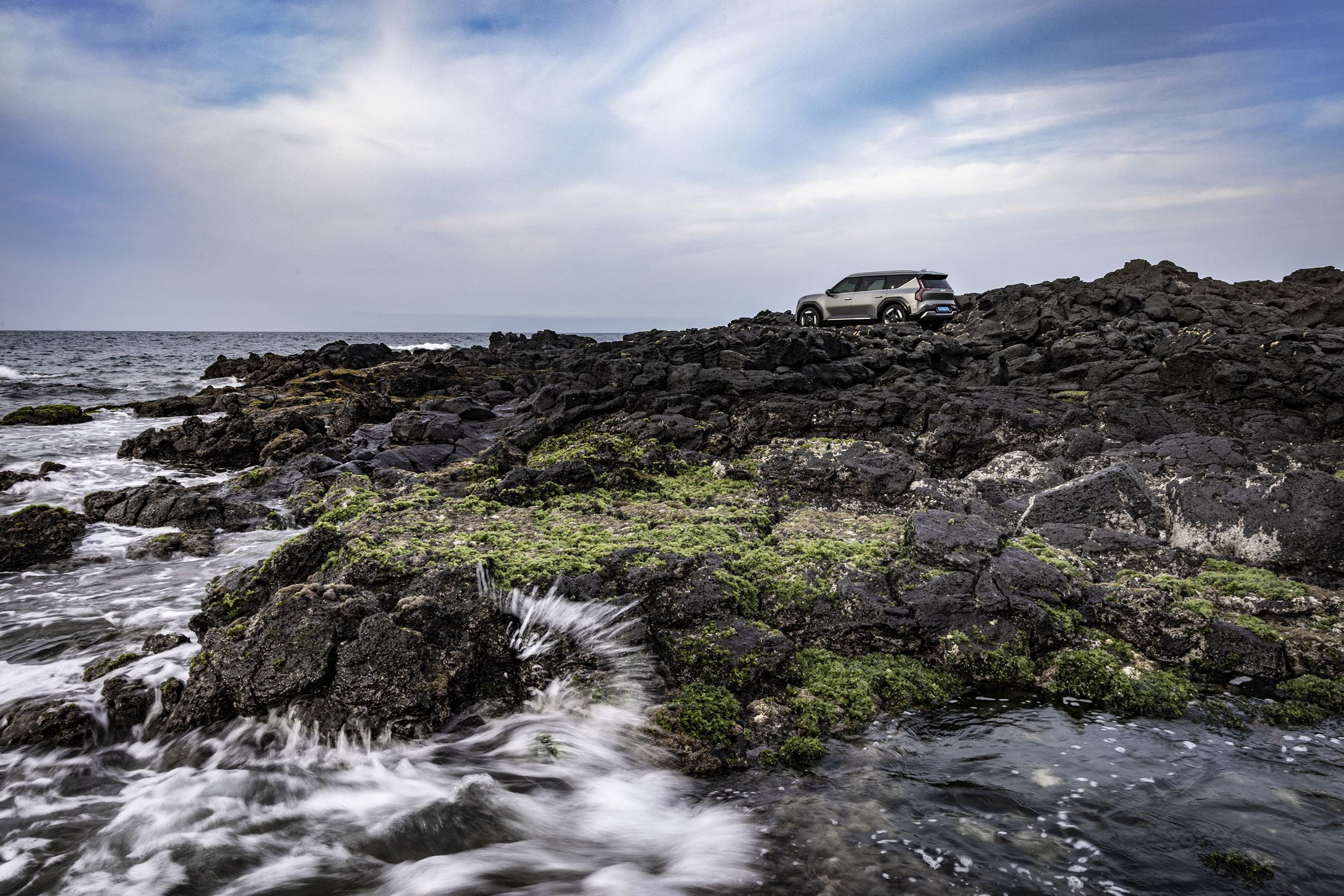 회색 SUV가 현무암 주변 바닷가에 정차한 후측면 모습