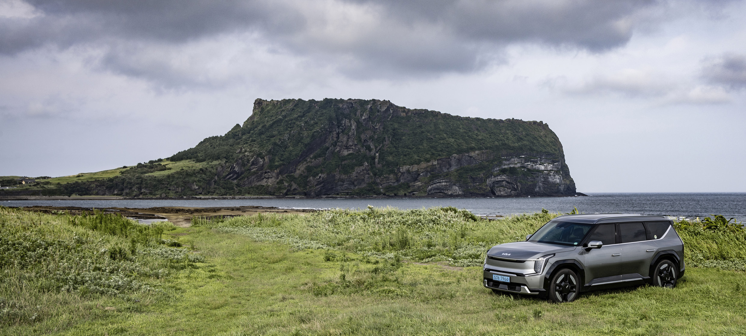 The front side of the gray SUV stopped against the backdrop of Seongsan Ilchulbong Peak