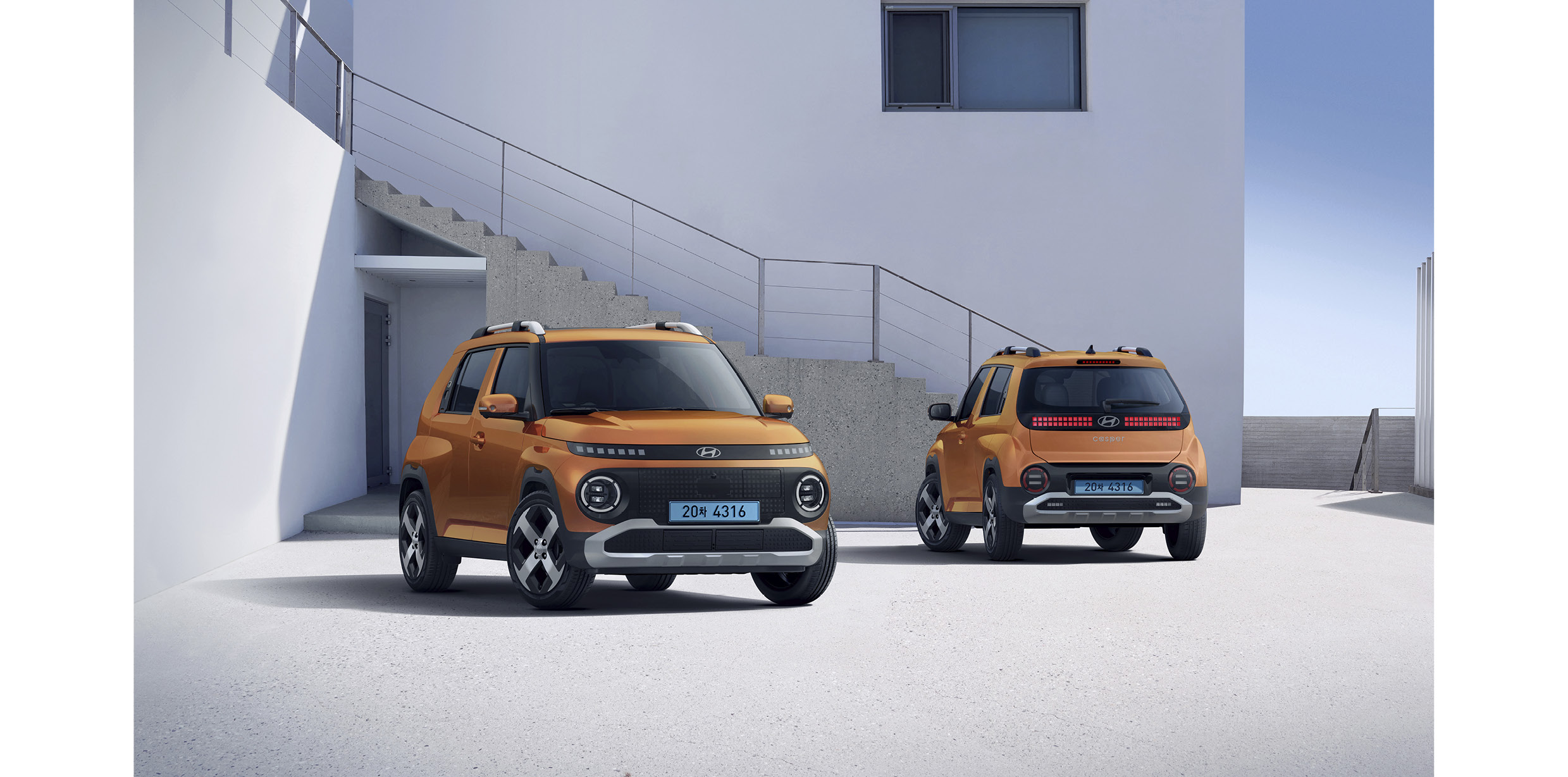 흰색 바탕의 건물 앞에 서있는 차량의 전측면과 후면 모습