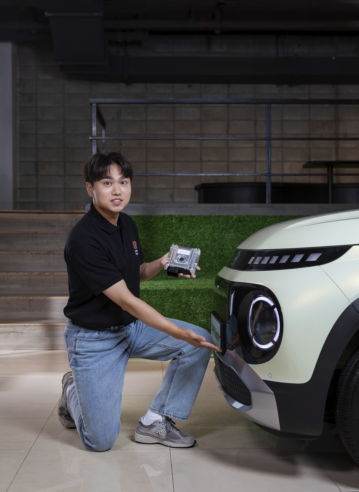 차량의 앞에서 센서를 가리키며 기능에 대해 설명하는 남자 연구원의 모습