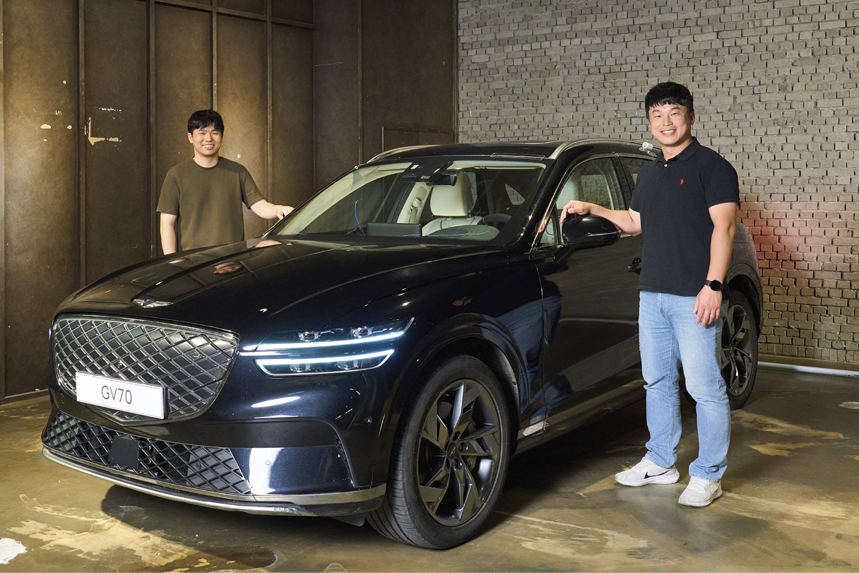 Two men standing side-by-side/left-hand in the vehicle