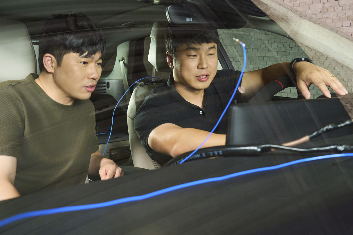 Two men sitting in the front seat, reaching for the crush pad and having a conversation